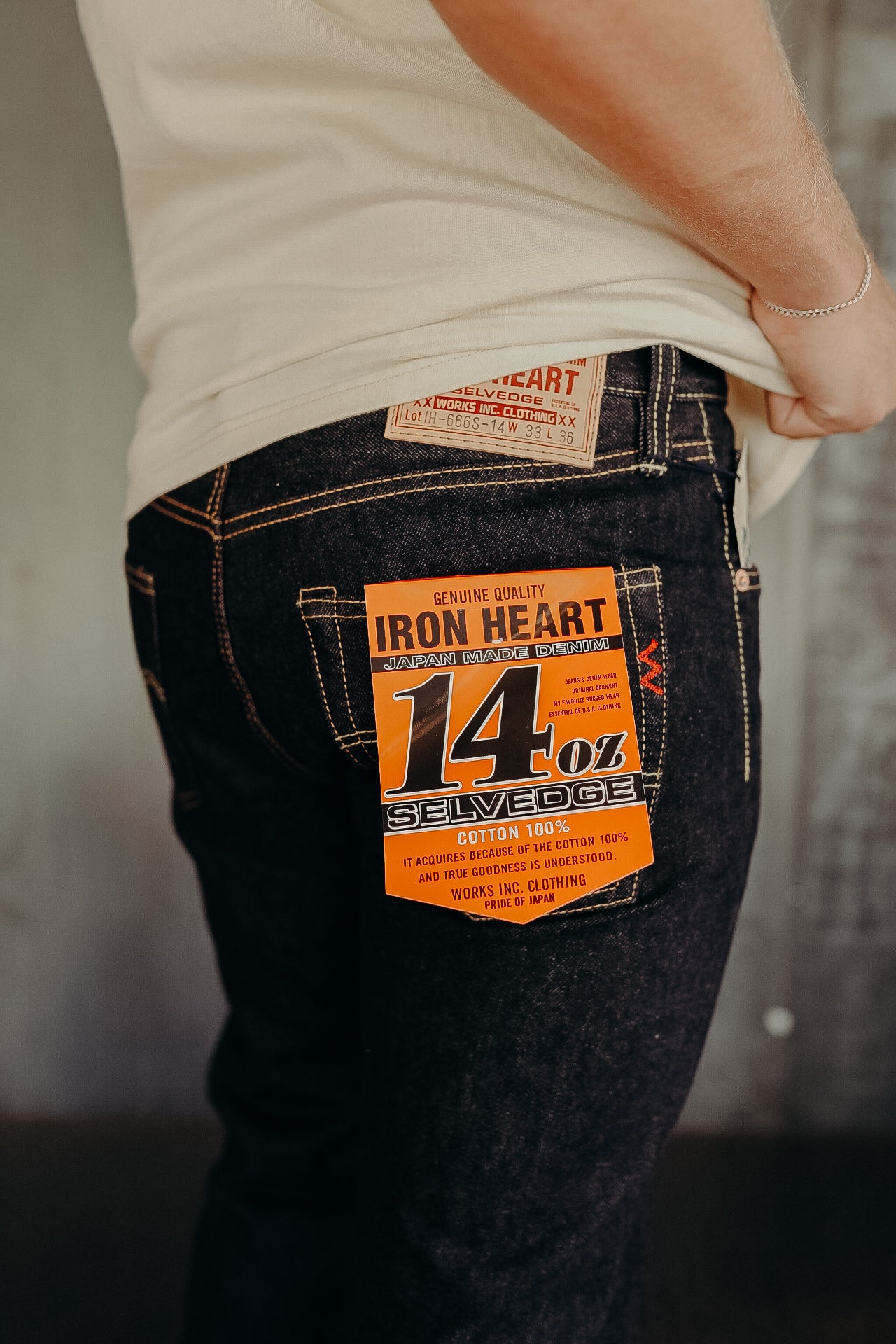 Close-up of person wearing dark blue Iron Heart 14oz selvedge Japanese denim jeans with orange label on back pocket
