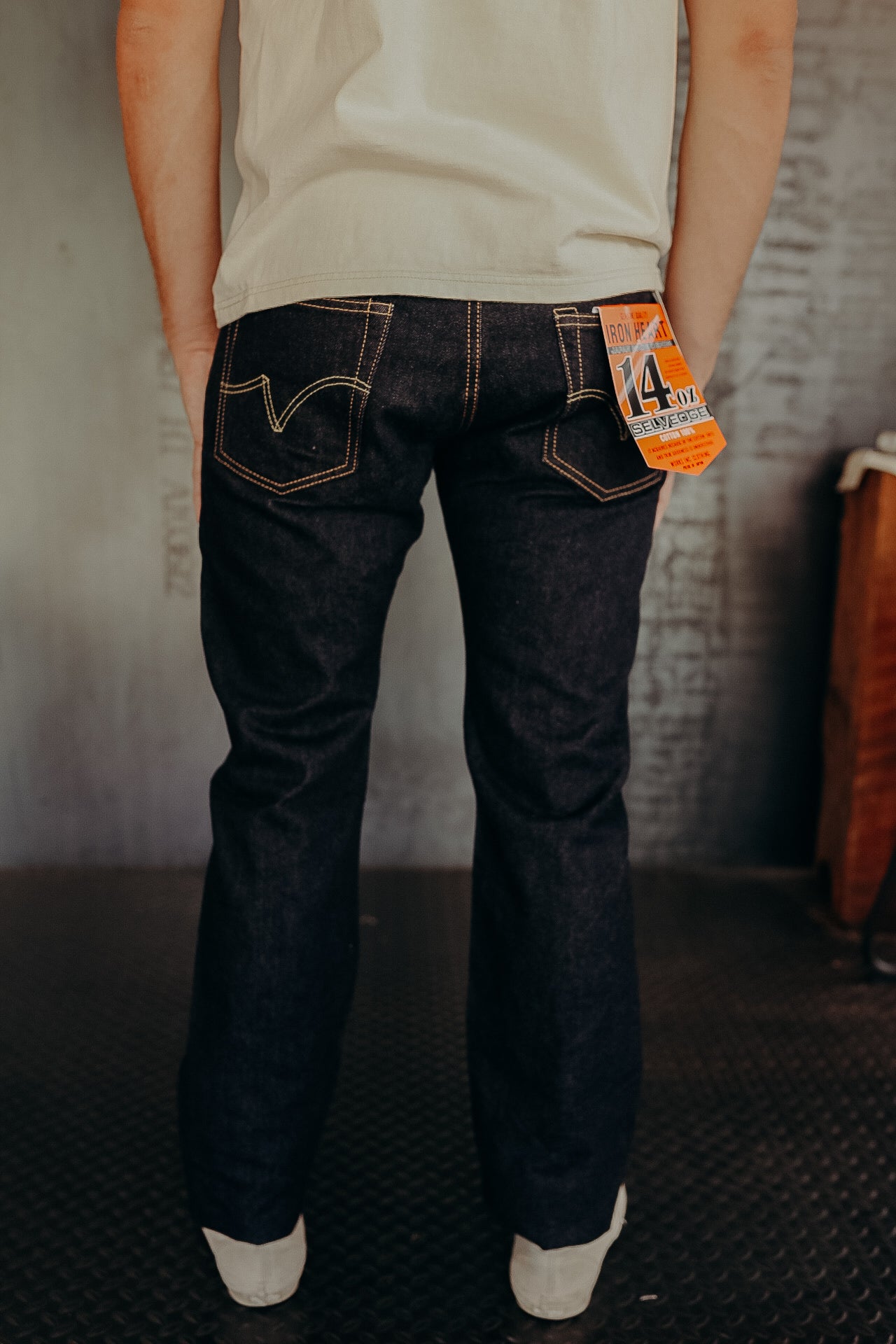 Back view of person wearing dark selvedge denim jeans with orange 14 oz Iron Heart label in industrial setting