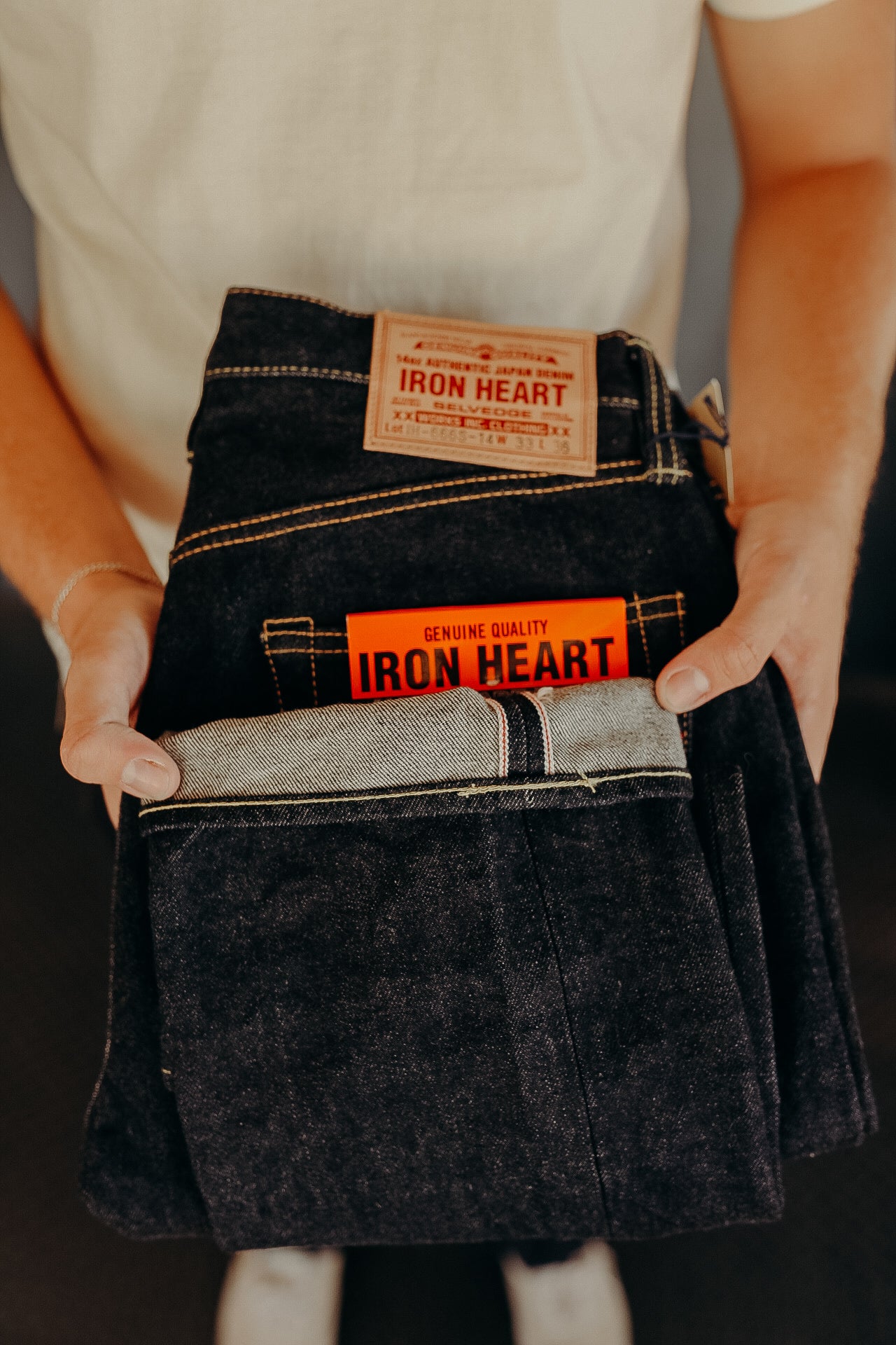 Person holding folded Iron Heart raw selvedge denim jeans with visible branding patches