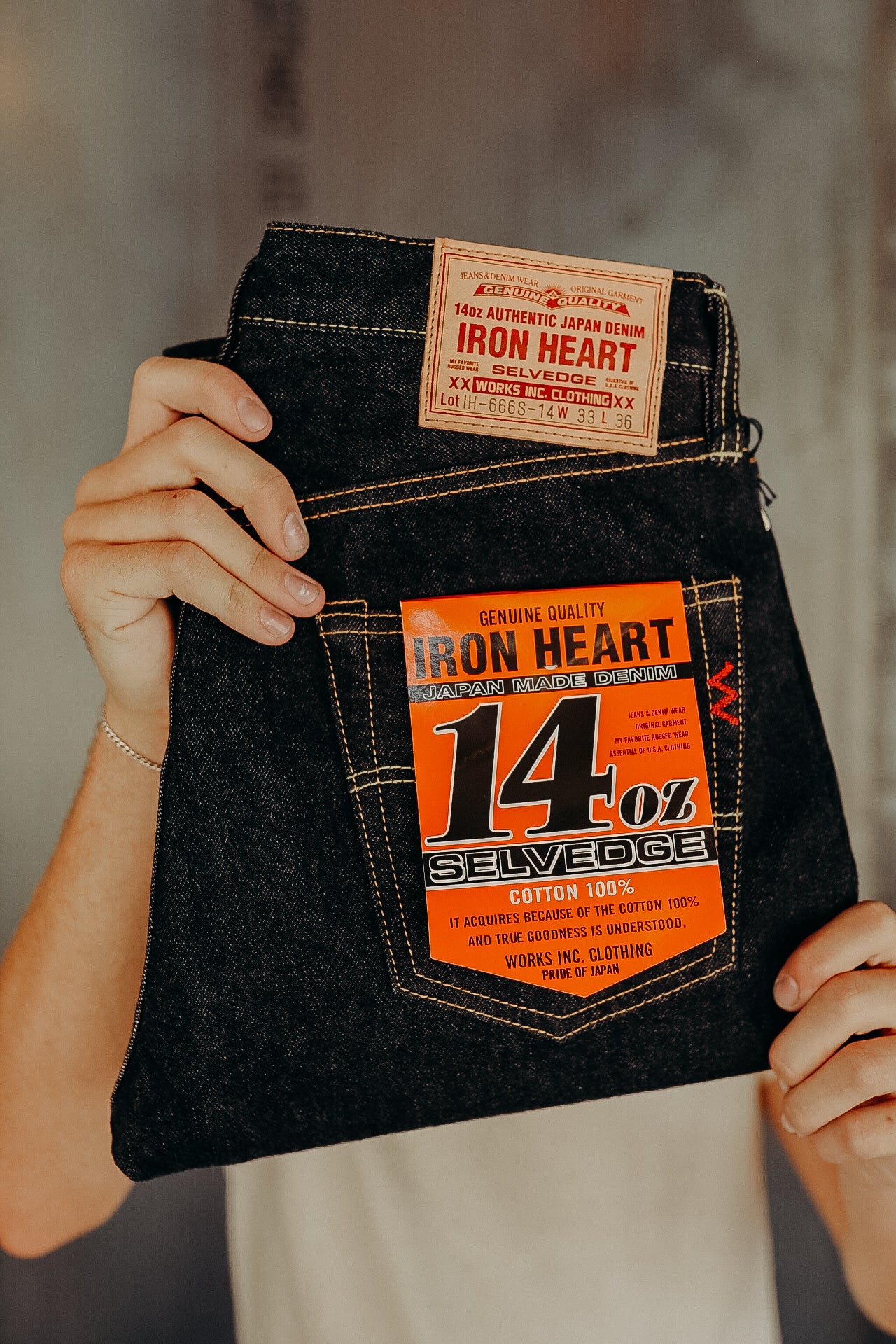 Person holding black Iron Heart 14oz selvedge Japanese denim jeans with orange and tan labels
