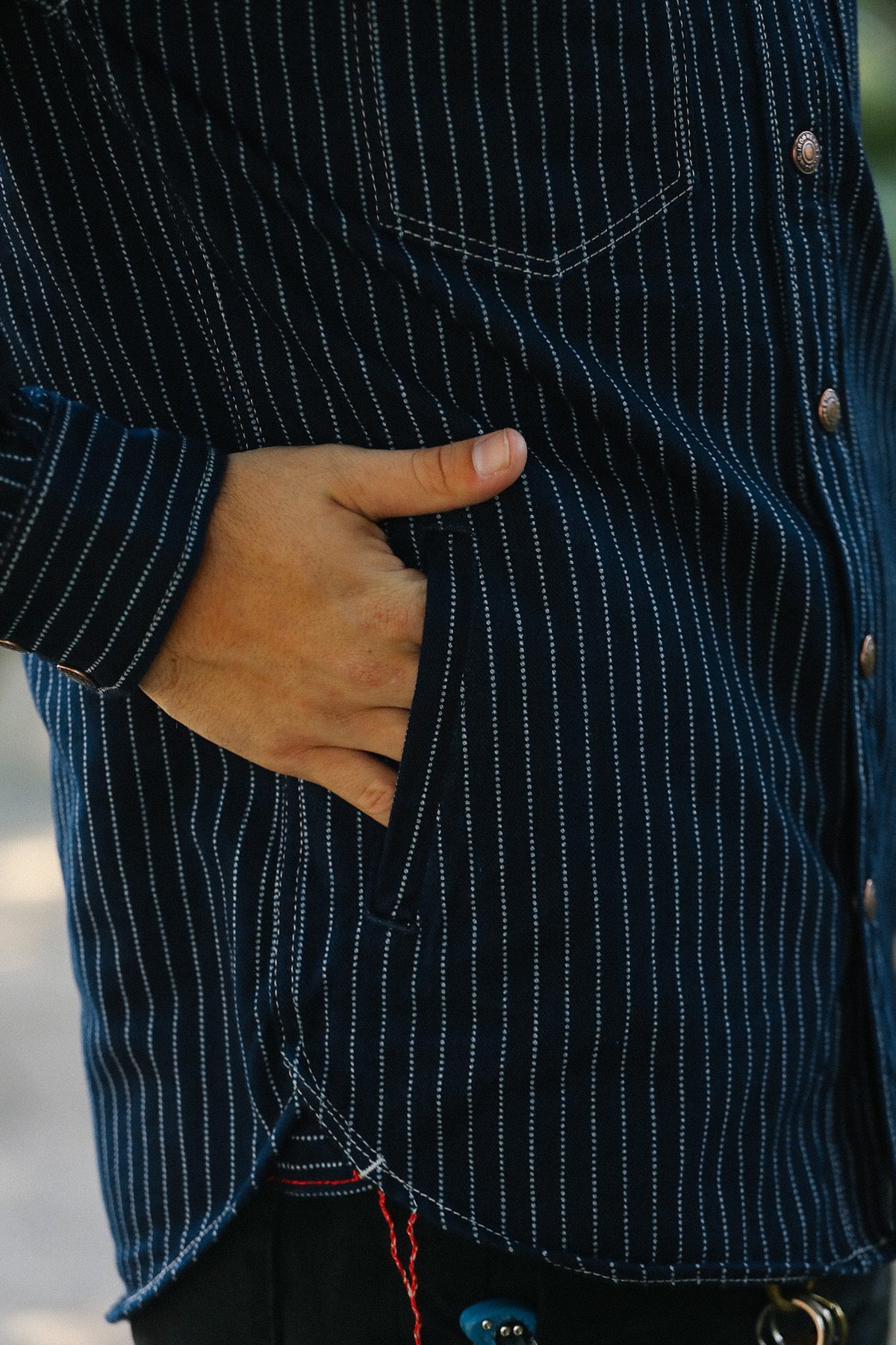 Close-up of a person wearing a dark navy pinstriped button-up shirt with a chest pocket and side pocket, with one hand in the pocket.