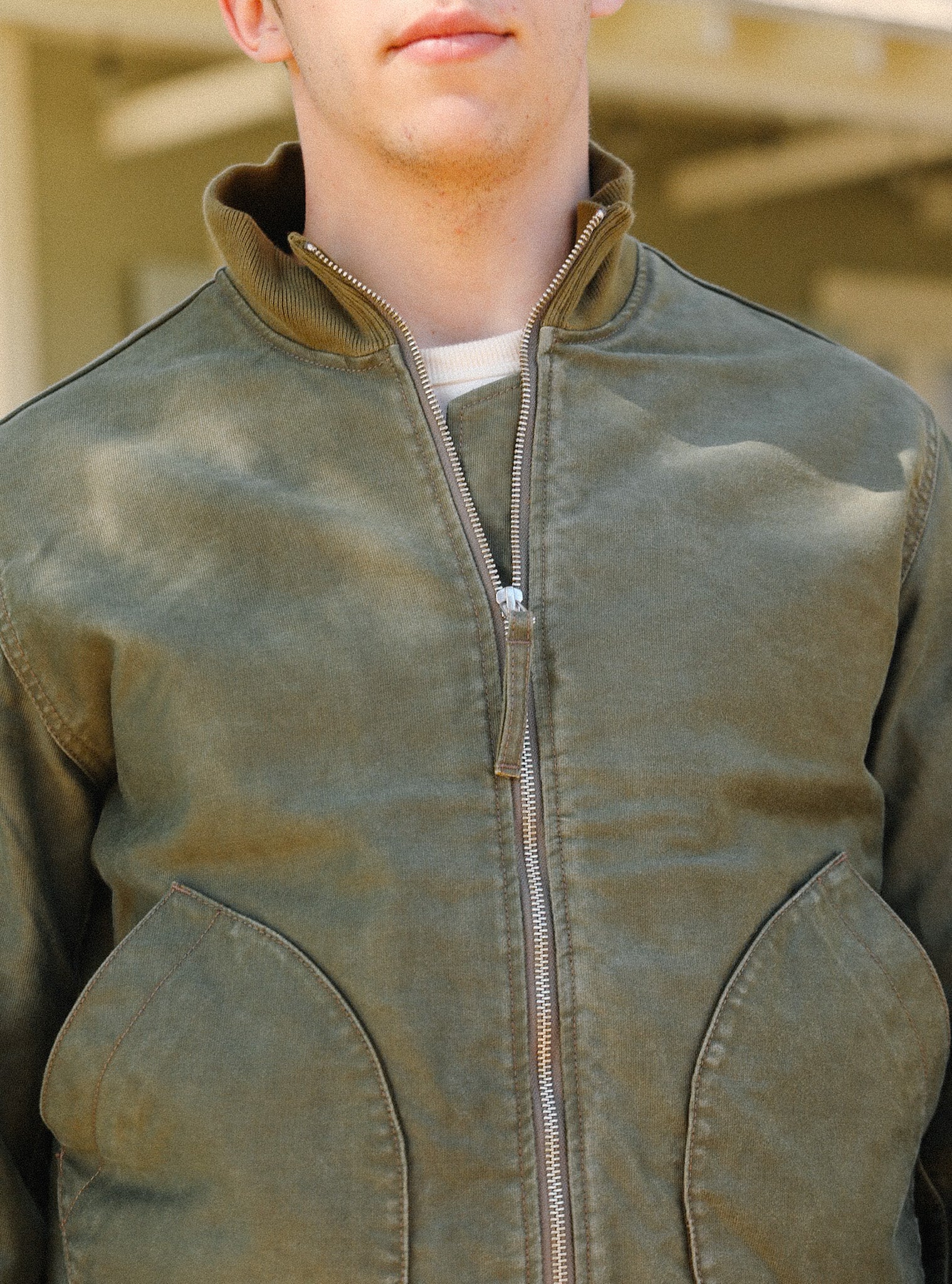 Close-up of a man wearing an olive green zip-up jacket with large front pockets and a ribbed collar