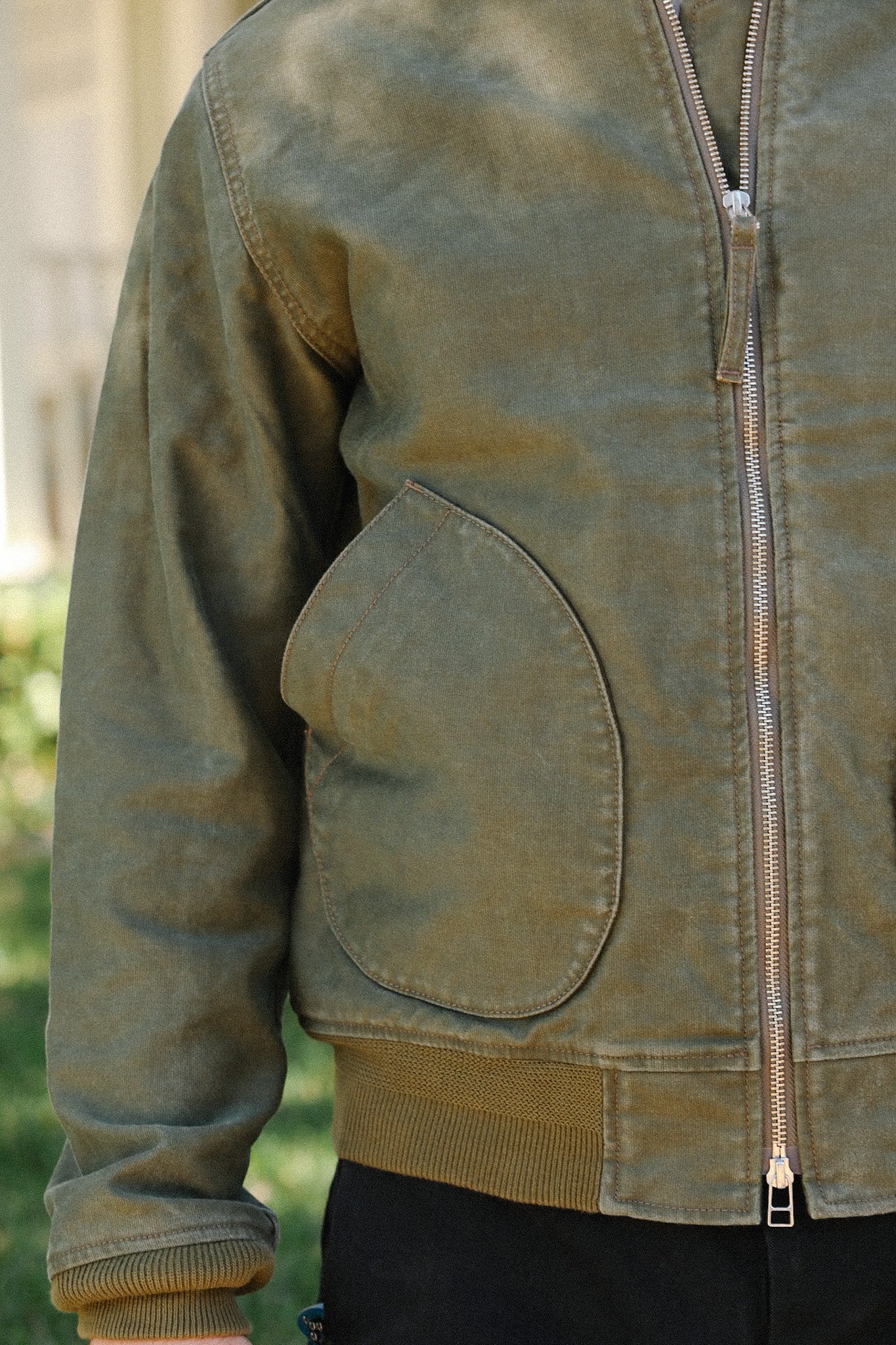 Close-up of rugged green canvas jacket with unique rounded pocket and zipper detail