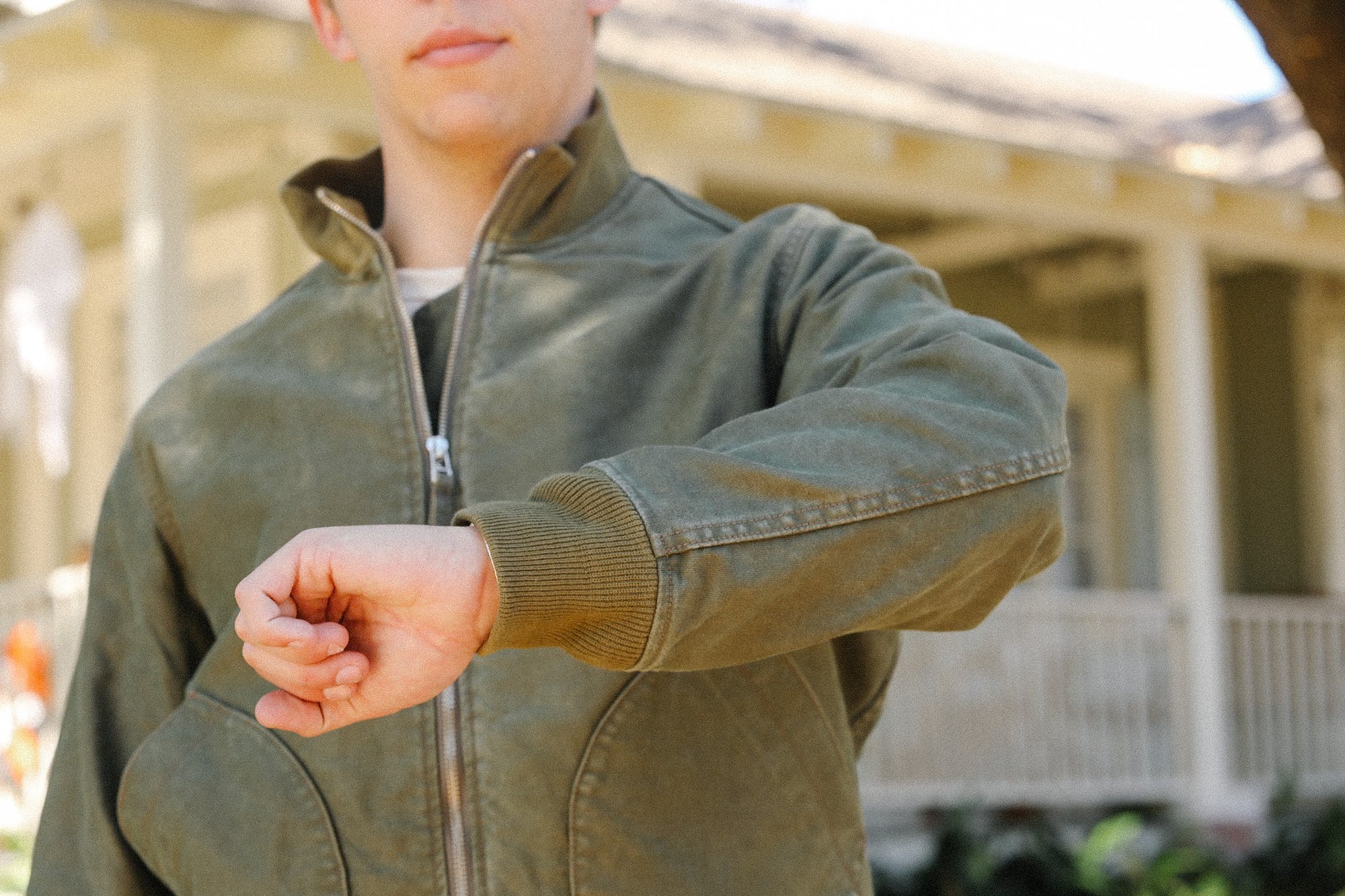 Person wearing olive green work jacket outdoors in front of beige building, showcasing durable outerwear