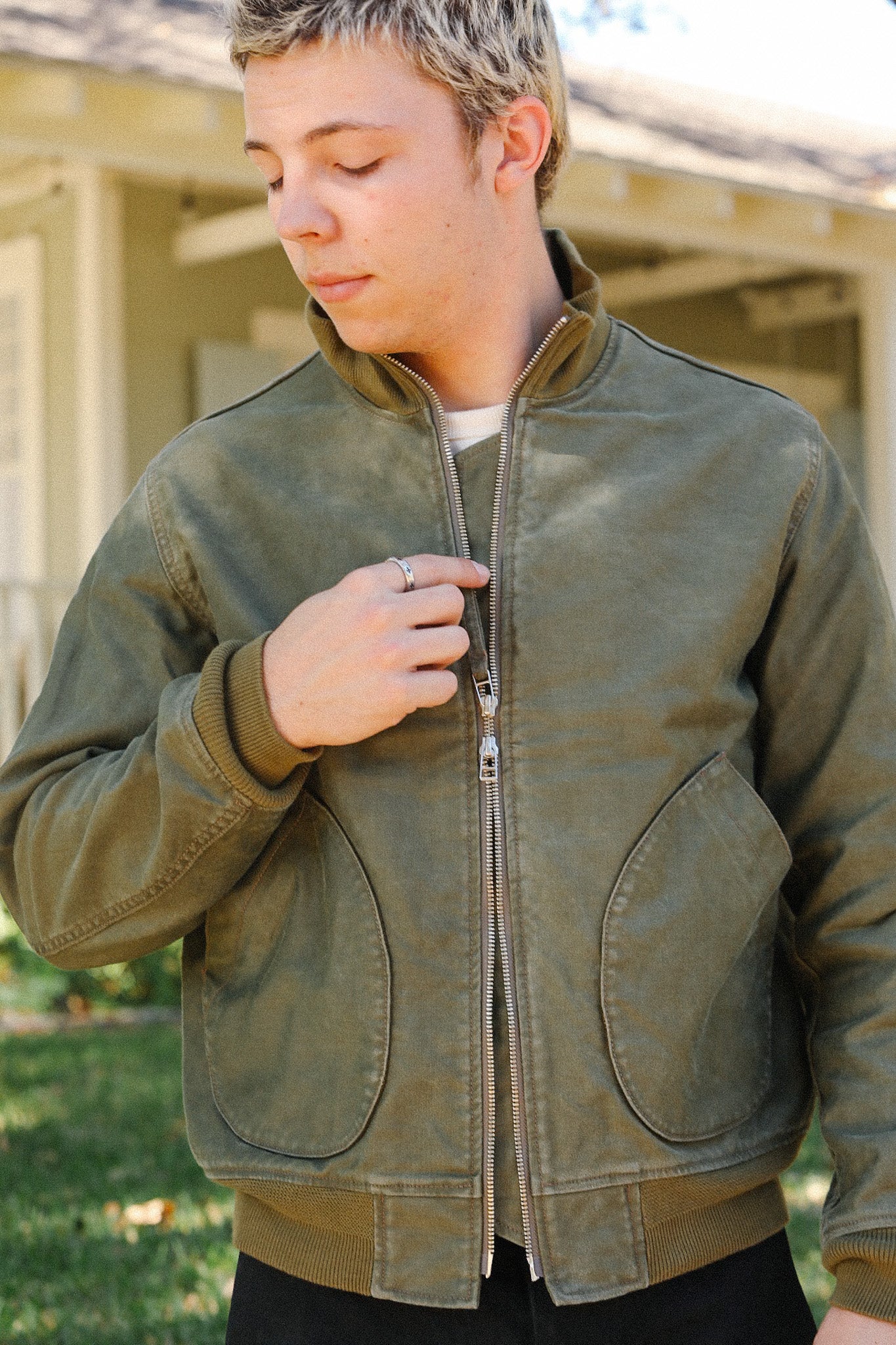Young man wearing olive green zip-up jacket with rounded pockets outdoors