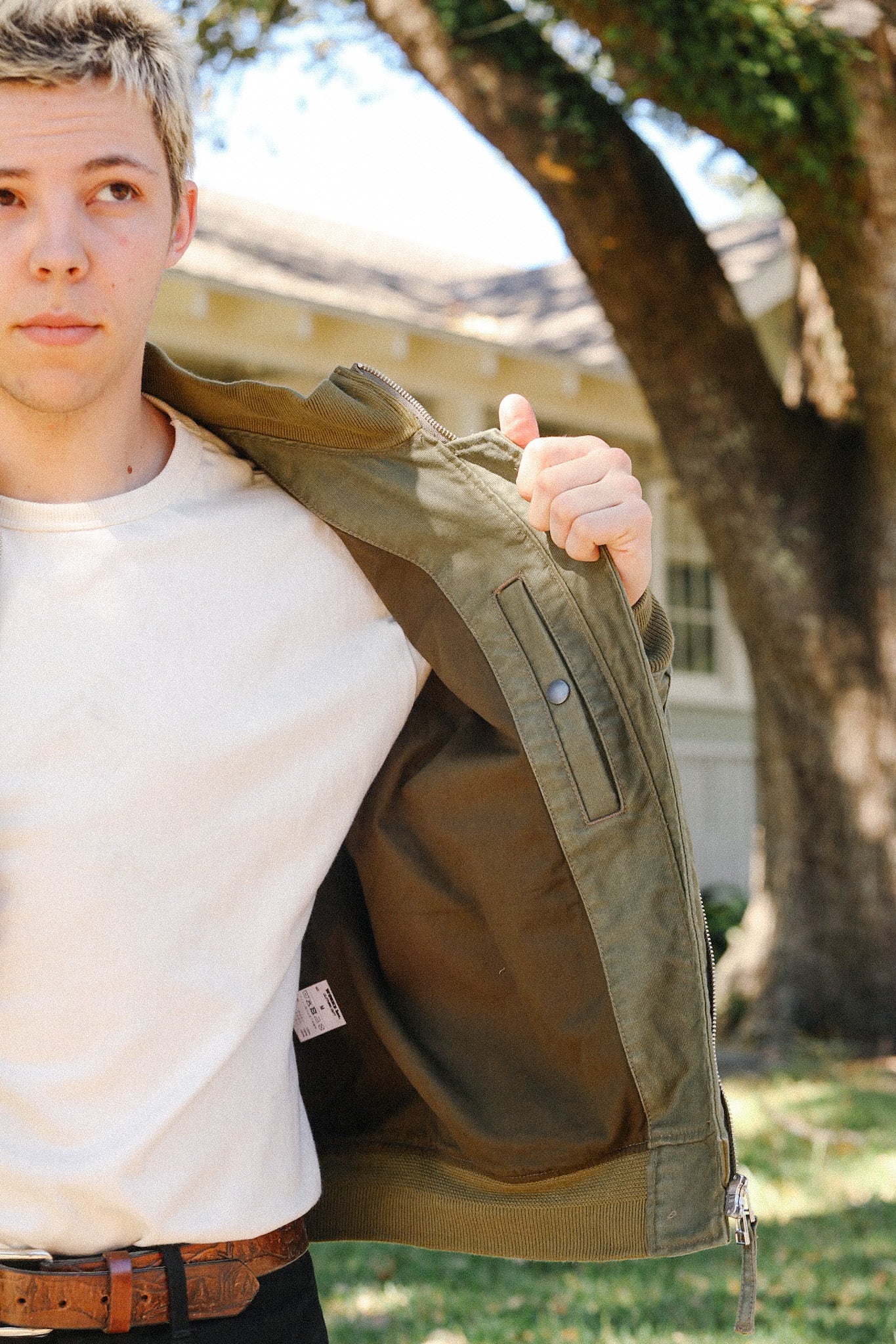 Young man outdoors wearing a white shirt and open olive green jacket showing interior pocket