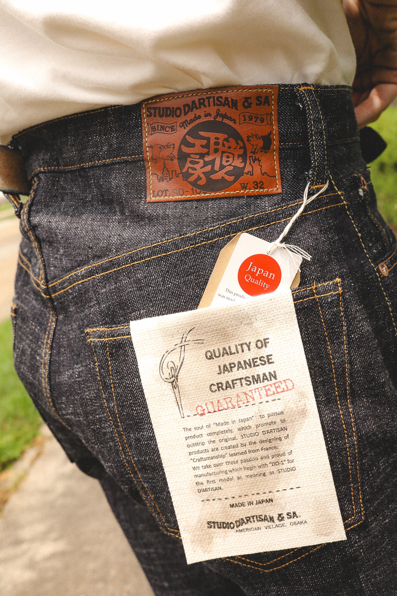 Close-up of dark denim jeans with Studio D'Artisan leather patch and Japan Quality tag, showcasing Japanese craftsmanship