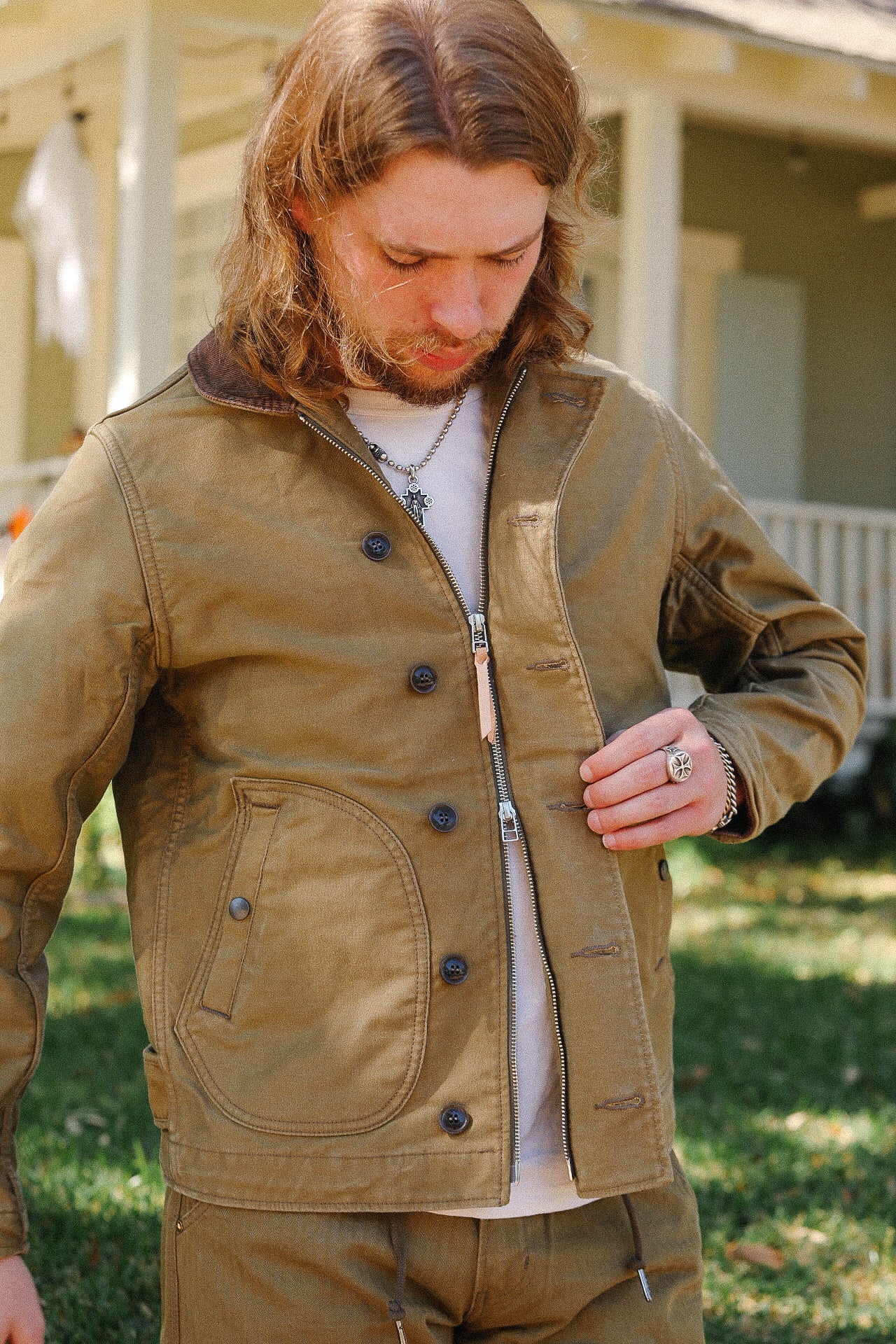 Man wearing brown canvas work jacket and pants outdoors near porch, showcasing rugged durable clothing