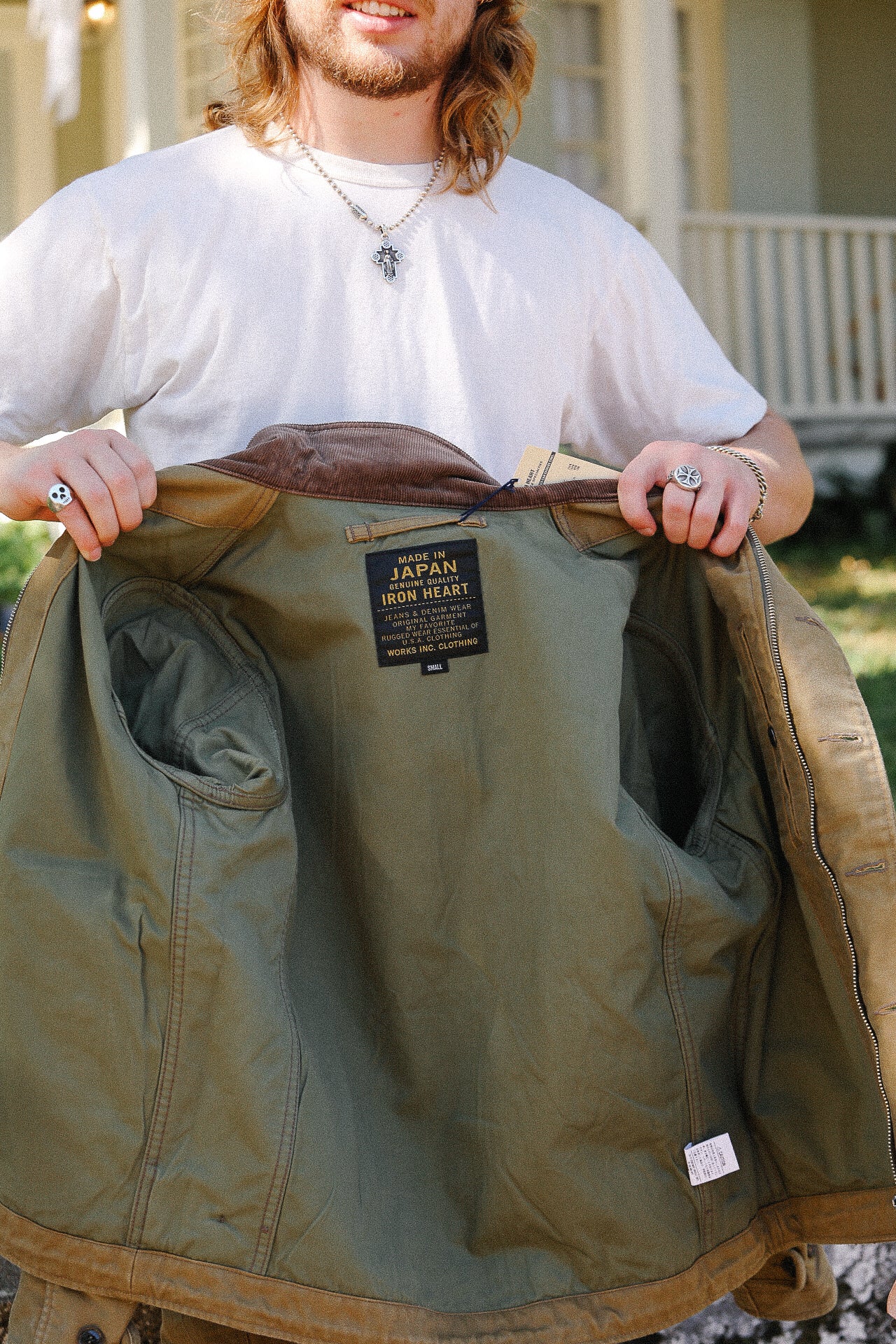 Person holding open an olive green Iron Heart jacket showing detailed inner label outdoors