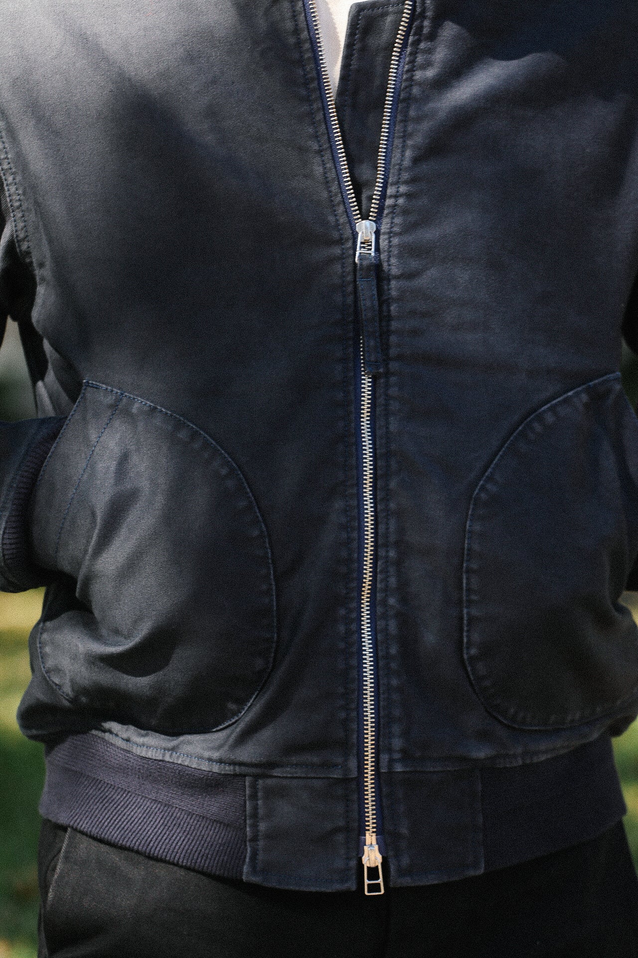 Close-up of person wearing navy blue zip-up jacket with rounded pockets and ribbed waistband