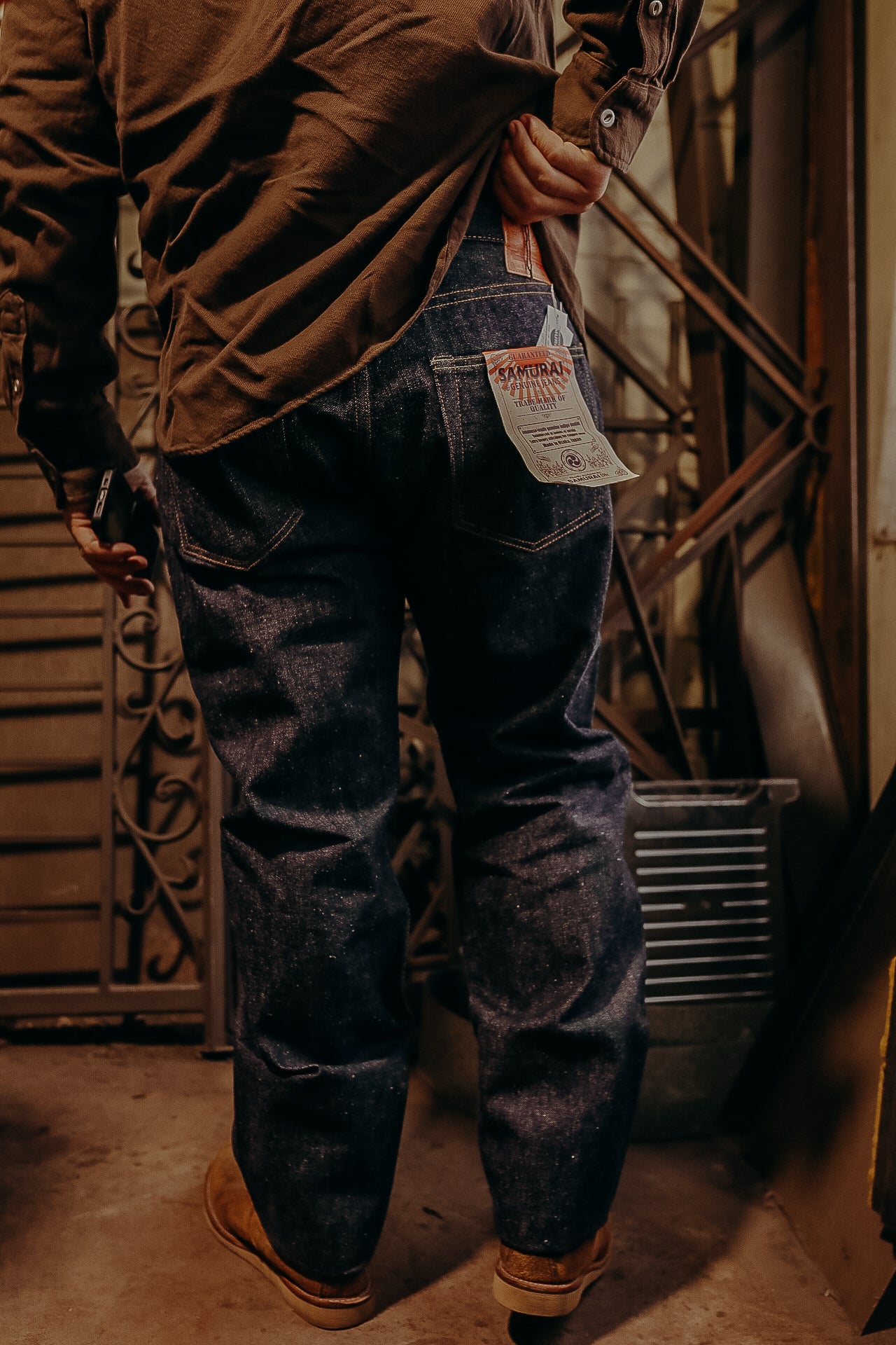 Person wearing dark Samurai brand raw denim jeans and brown shoes in industrial setting