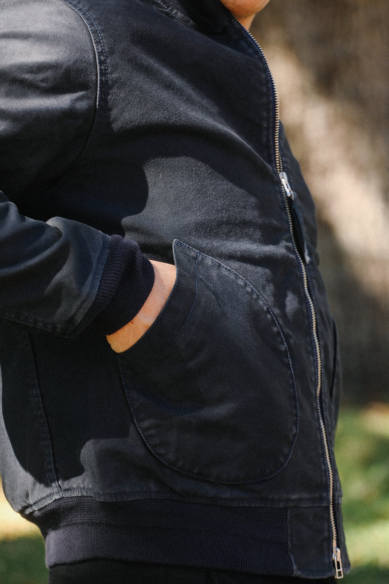 Close-up of person wearing black Iron Shop Provisions jacket with zip and rounded side pocket outdoors