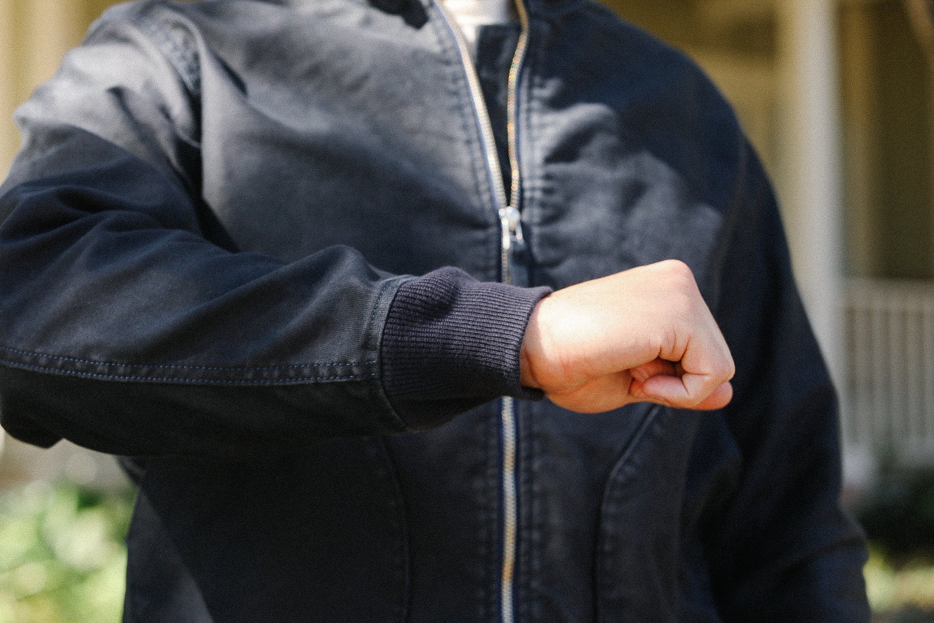 Person wearing a black zip-up jacket with ribbed cuffs showing a clenched fist in an outdoor setting