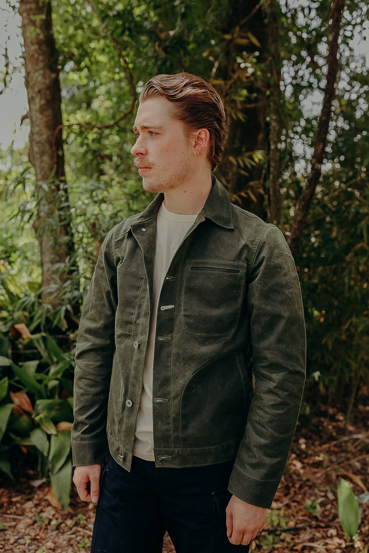 Man wearing dark green work jacket over white shirt standing in wooded outdoor setting
