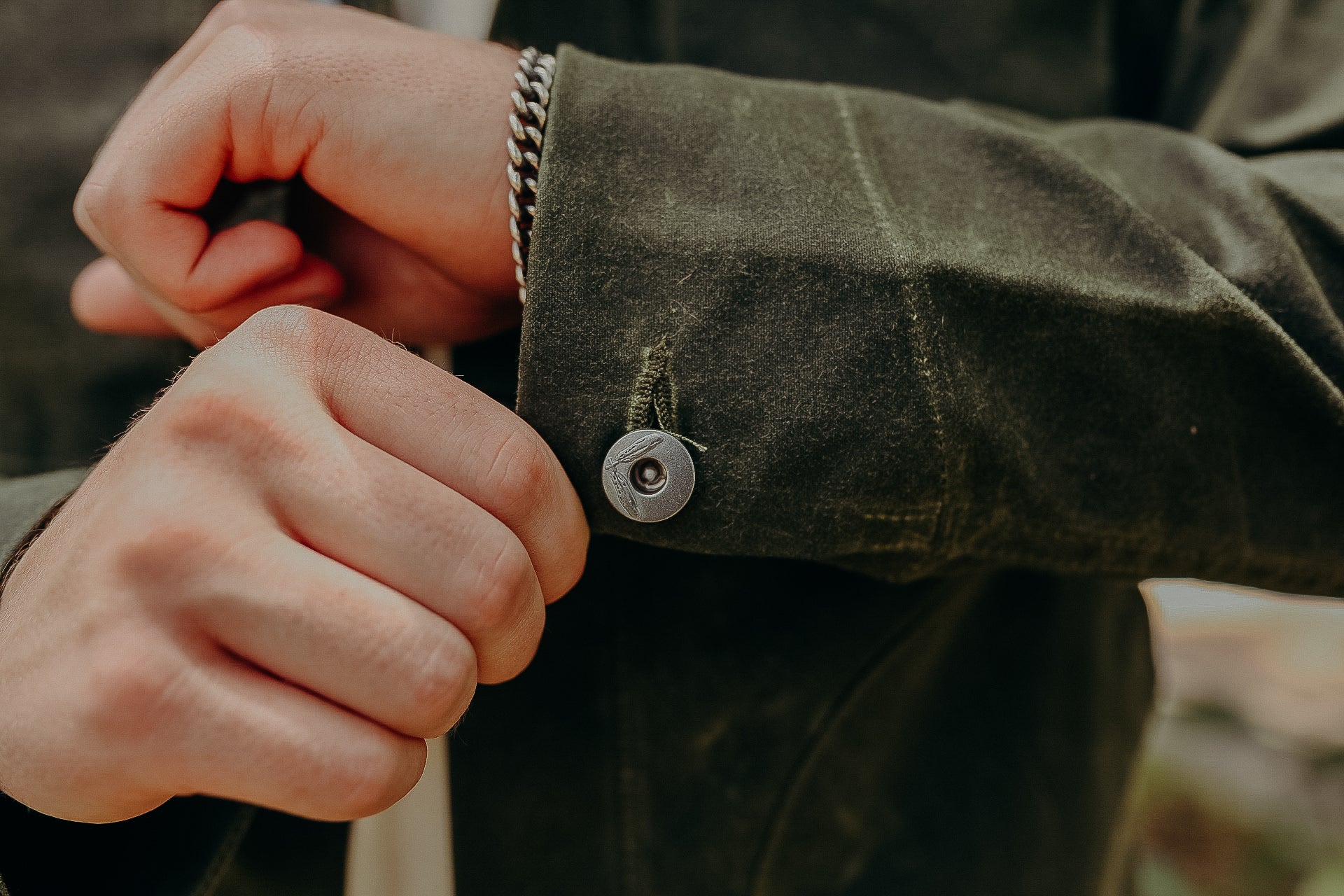 Close-up of hands buttoning olive green jacket cuff with metal button and silver bracelet