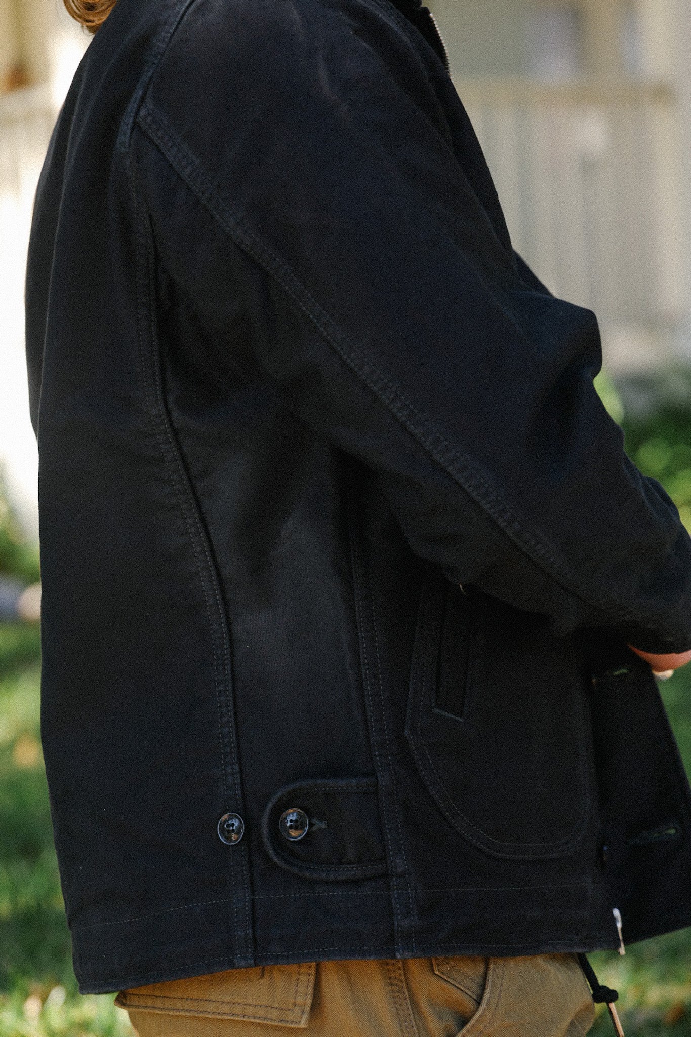 Close-up of black canvas work jacket with button and pocket detail on person outdoors