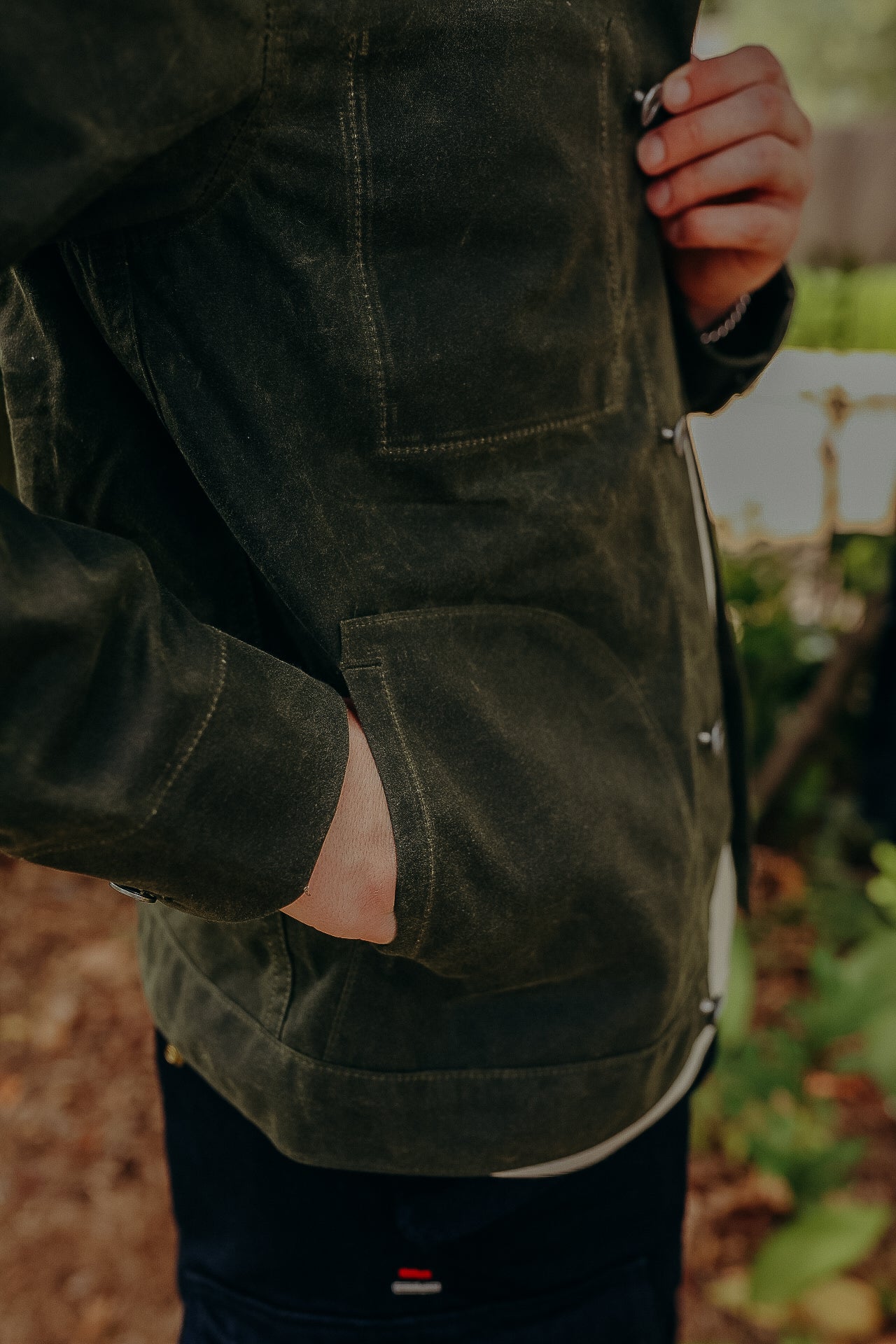 Close-up of a person wearing a rugged olive green work jacket with functional pockets at Iron Shop Provisions