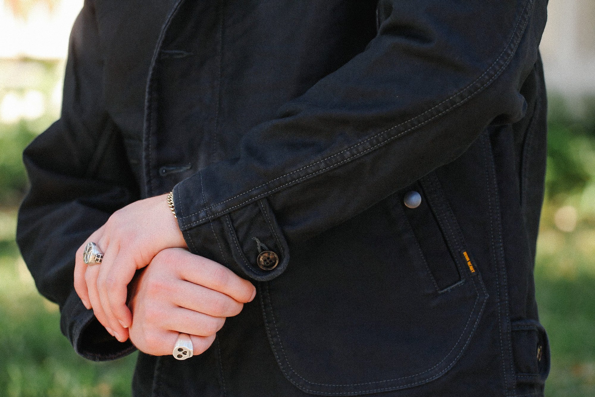 Close-up of hands with silver rings and bracelet on black rugged work jacket pocket