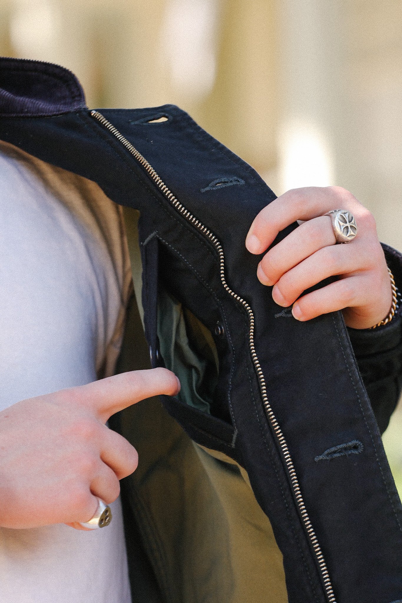 Person wearing a white shirt showing the inner pocket of a black zip-up jacket with silver zipper and detailed stitching