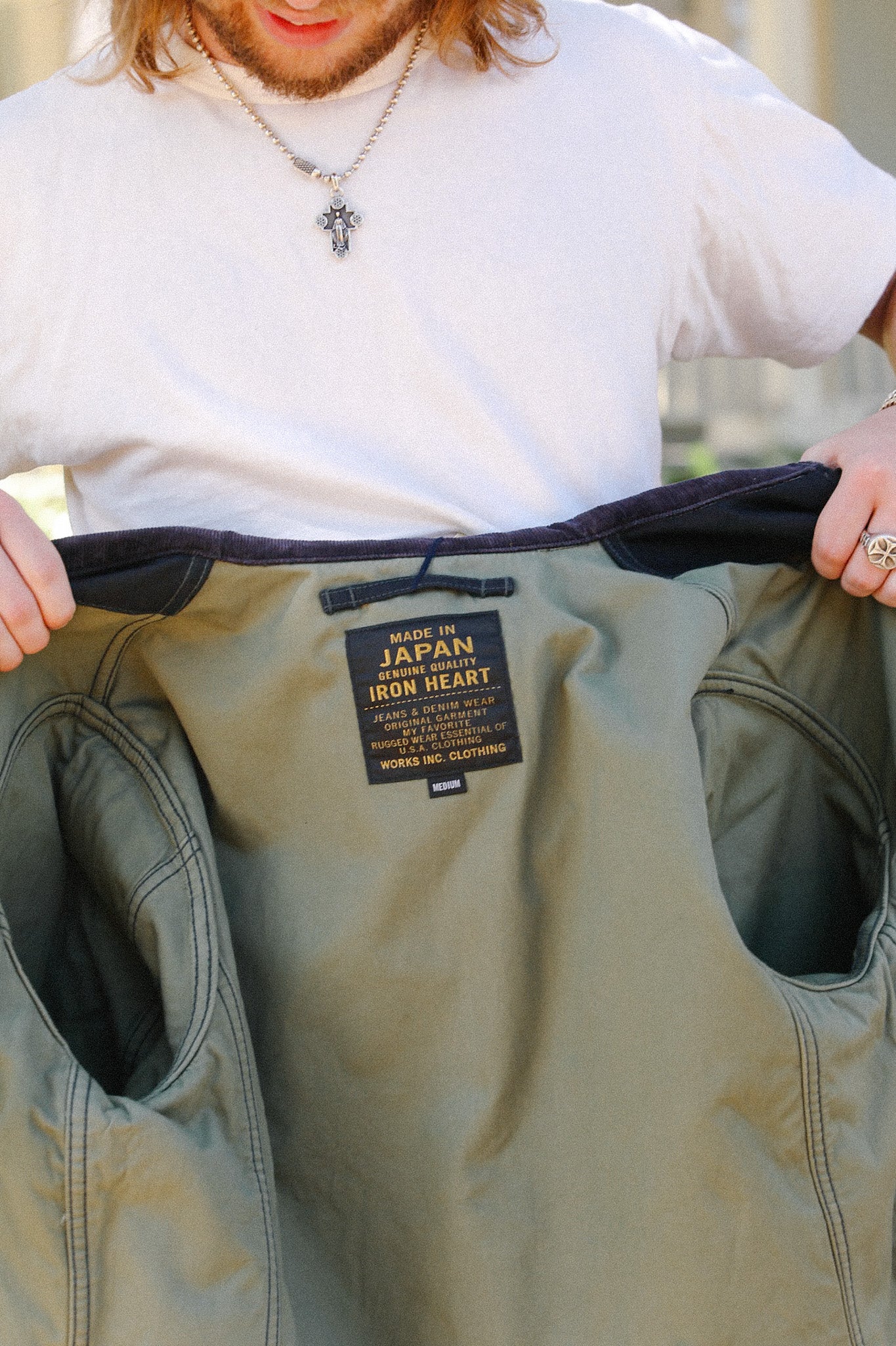 Close-up of a person holding open an Iron Heart green jacket showing a 'Made in Japan' label