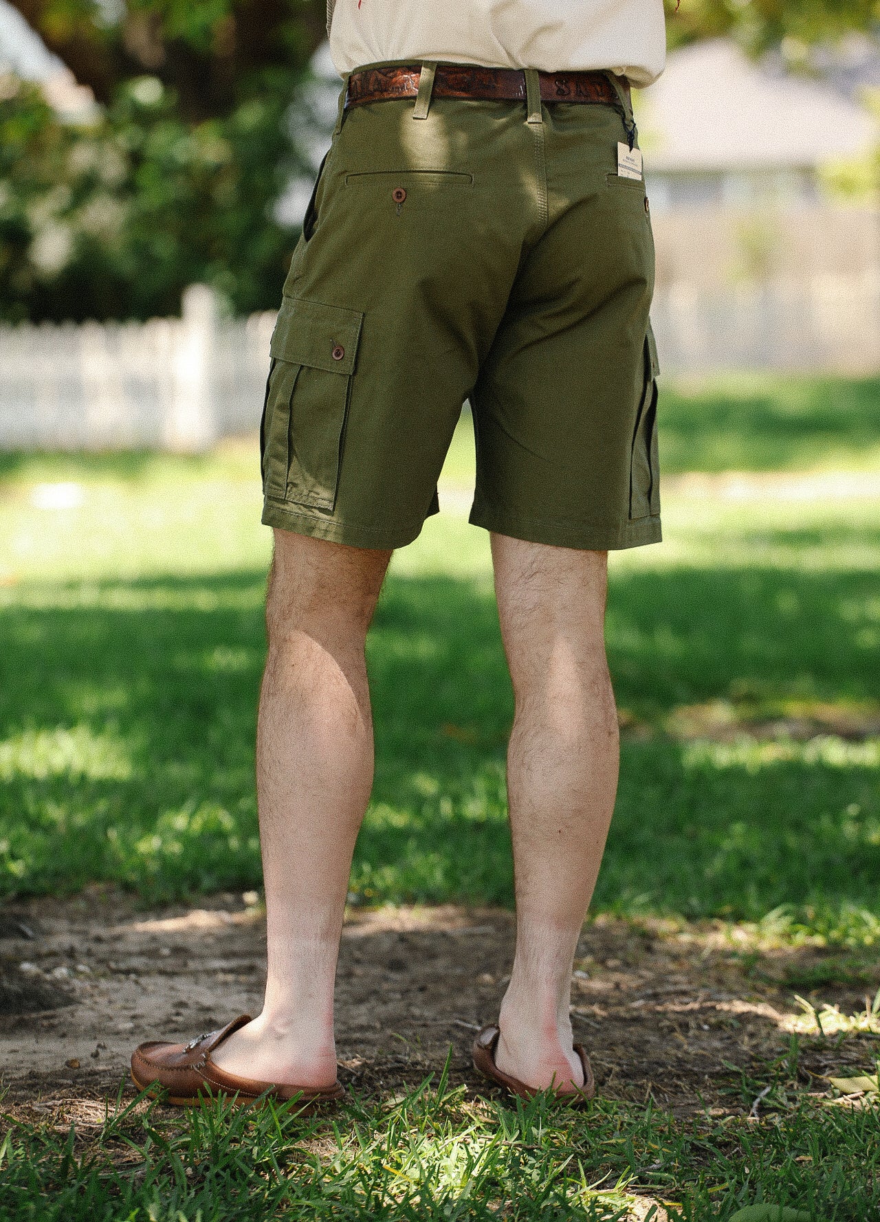 Rear view of man wearing olive green cargo shorts and brown leather slip-on shoes in a sunny park
