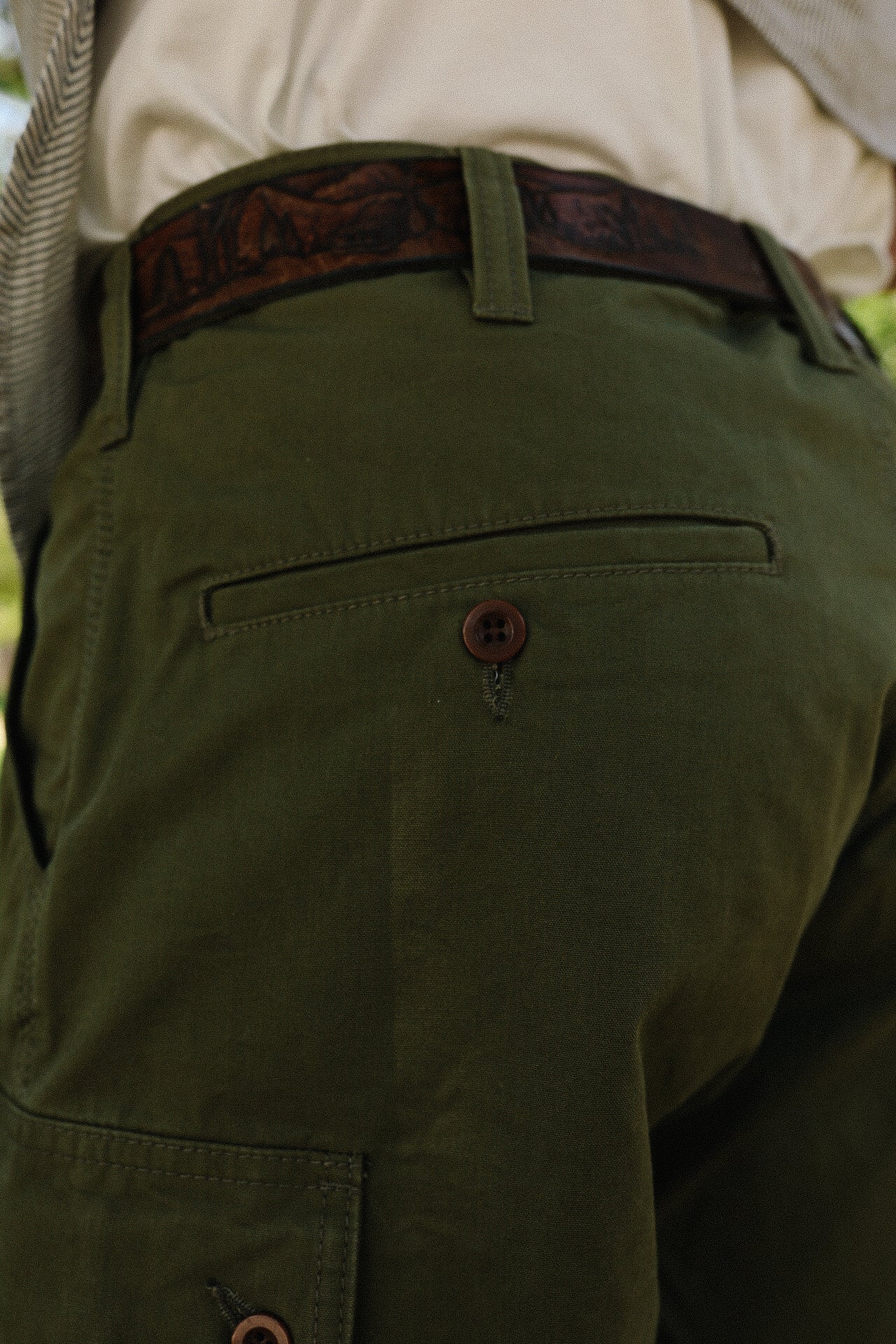 Close-up of olive green pants with brown button and leather belt from Iron Shop Provisions