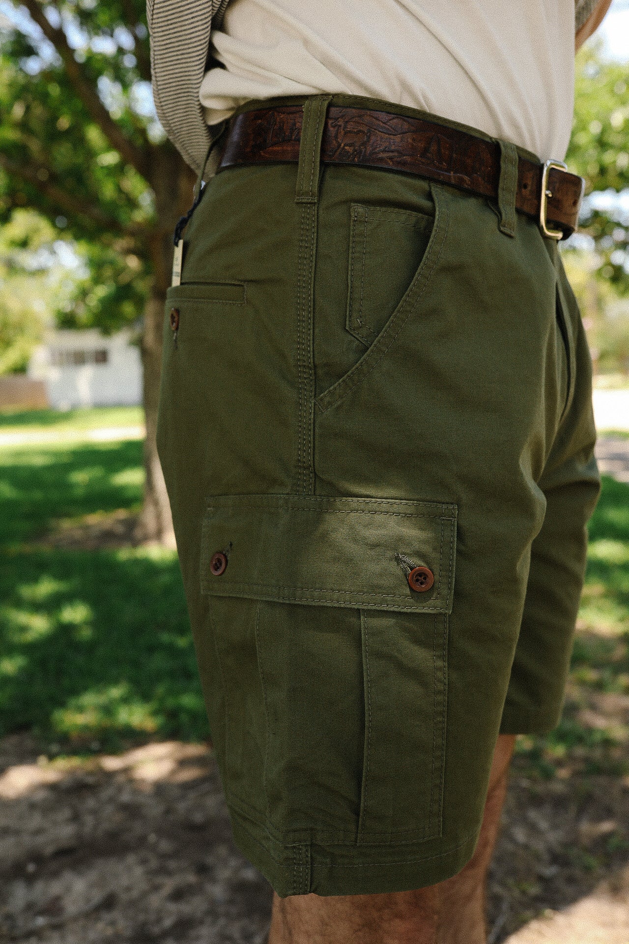 Close-up of men's olive green cargo shorts with buttoned pockets and brown leather belt outdoors