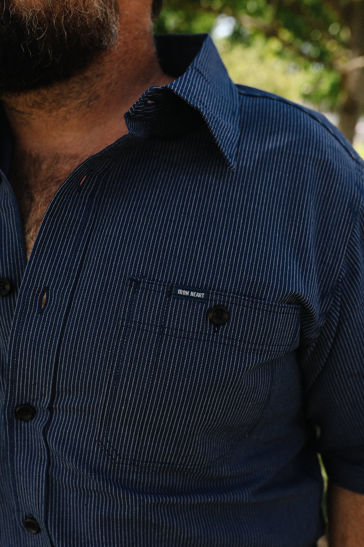 Close-up of man wearing a navy blue Iron Heart striped button-up shirt outdoors