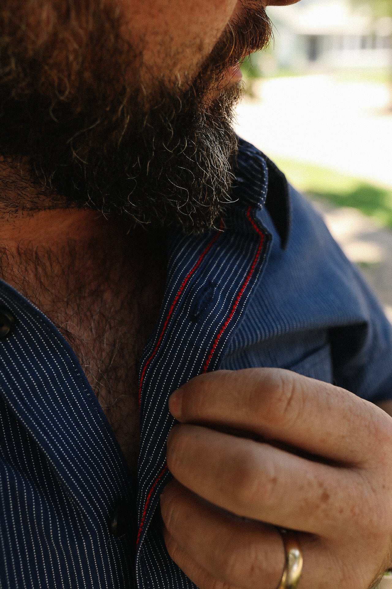 Close-up of man with full beard wearing a blue pinstripe shirt with red trim detail