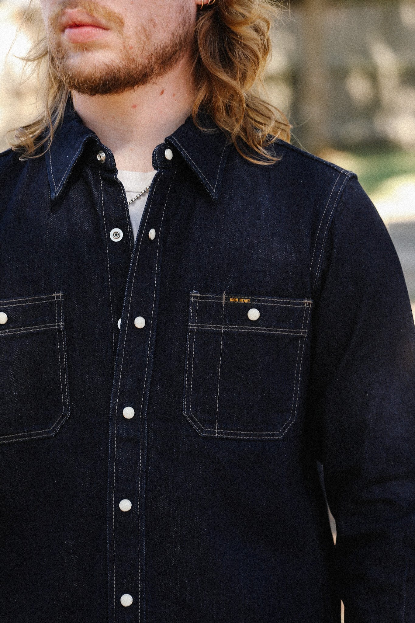 Close-up of man wearing dark denim shirt with white snap buttons and chest pockets outdoors