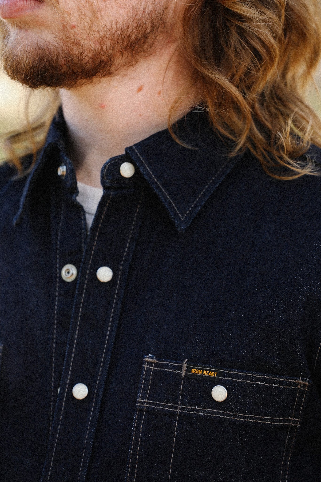 Close-up of person wearing dark denim Iron Heart shirt with white snap buttons and chest pocket detail