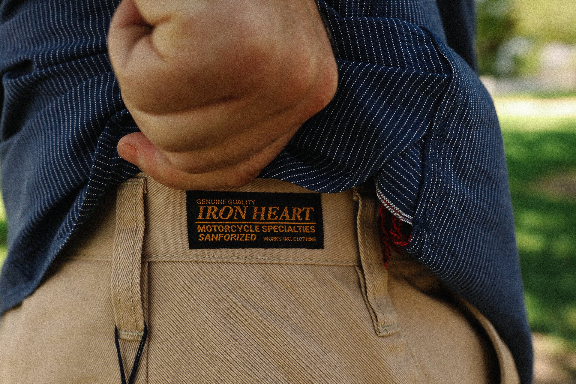 close-up of hand lifting blue pinstripe shirt pocket to reveal iron heart motorcycle jeans label