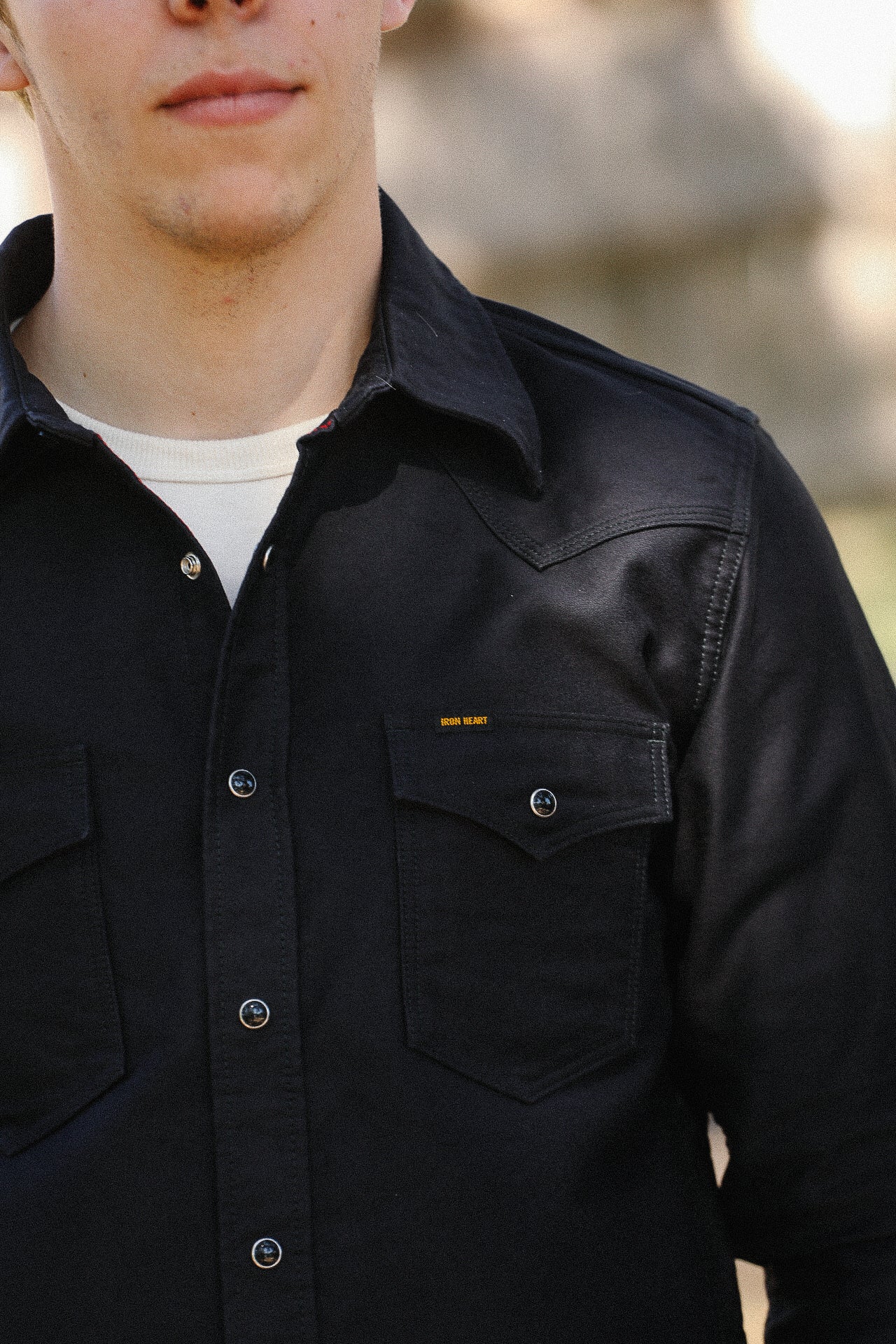 Close-up of a man wearing a black Iron Heart button-up shirt with flap chest pockets outdoors