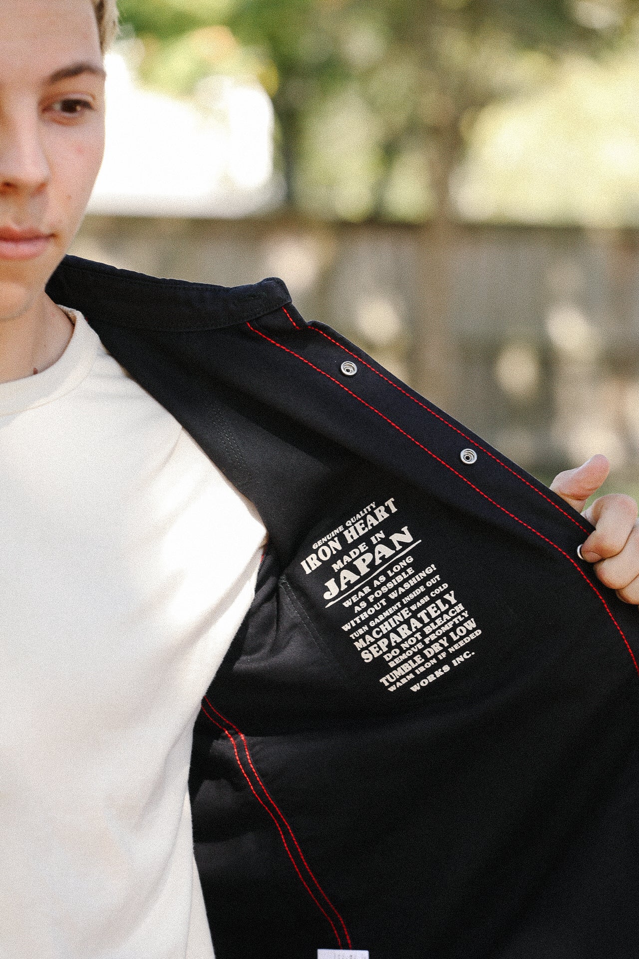 Close-up of a person showing the inside label of a black Iron Heart jacket with red stitching, made in Japan
