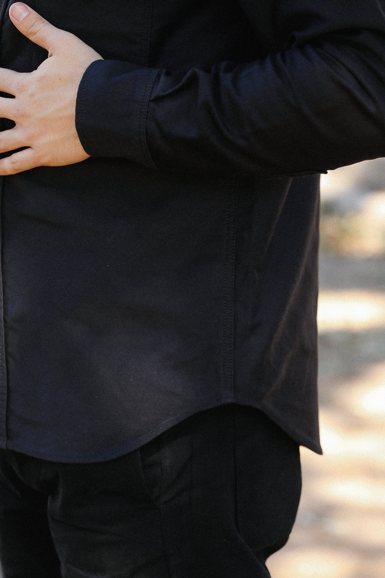 close-up of a person wearing a black long-sleeve shirt and black pants with hand resting on the side