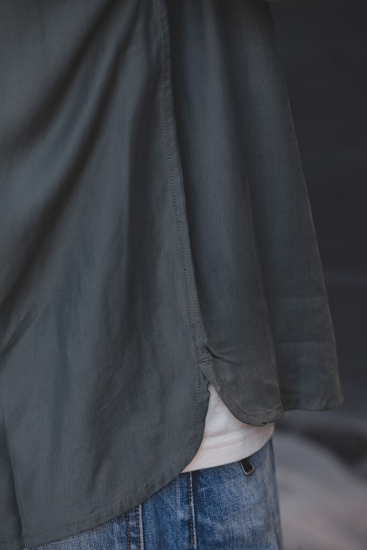 Close-up of a person wearing a dark charcoal gray linen shirt over a white undershirt and blue jeans.