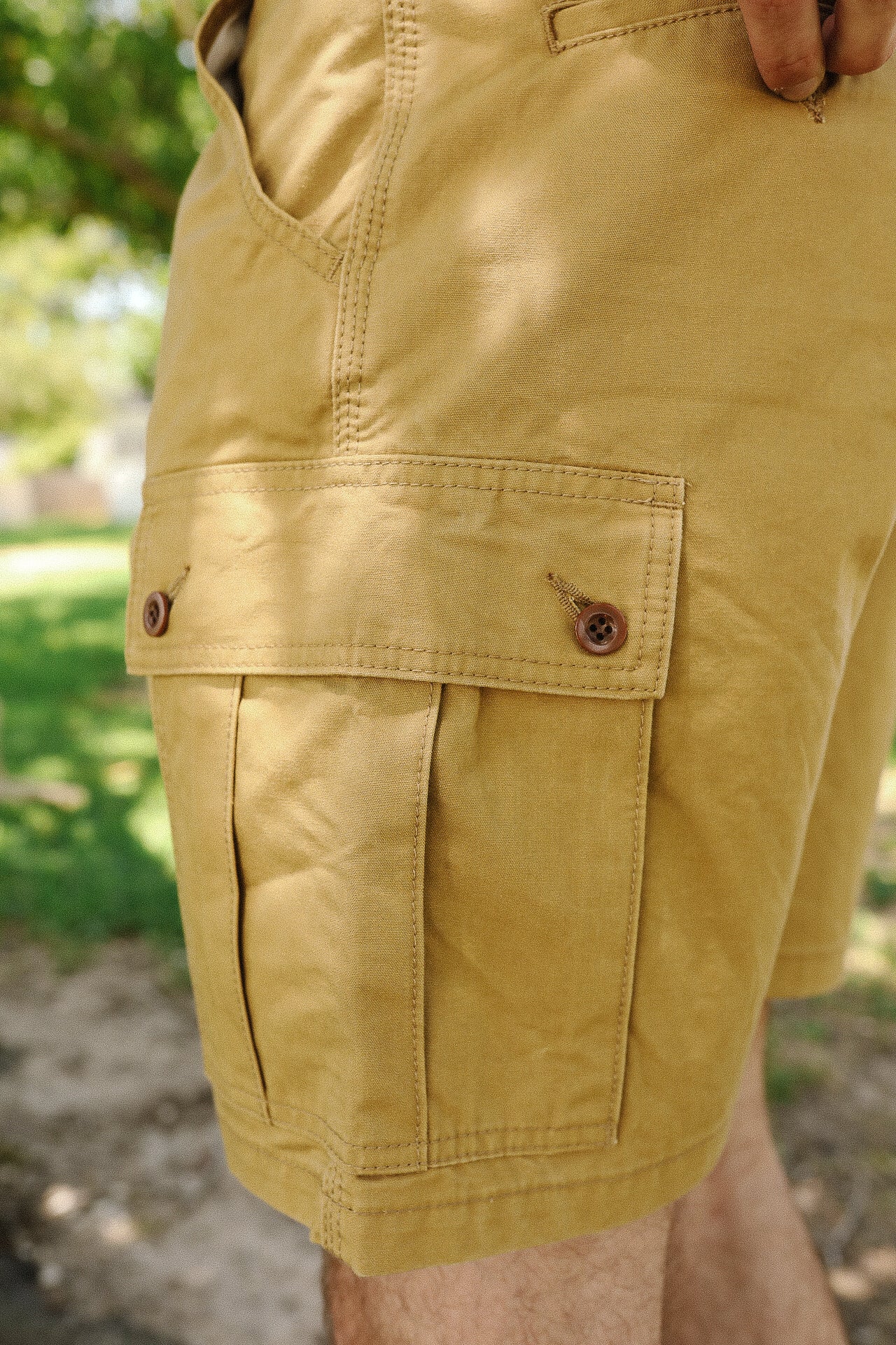 Close-up of mustard yellow cargo shorts with buttoned flap pocket on a person outdoors