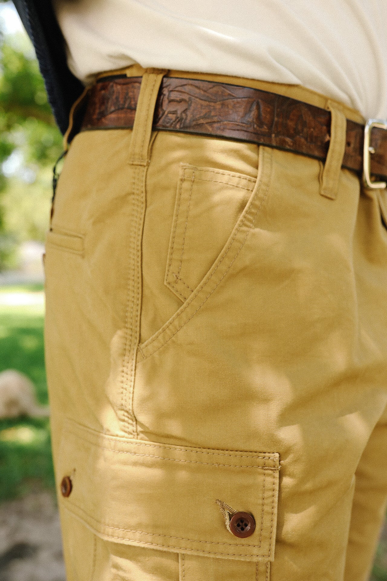 Close-up of tan work pants with side pocket and engraved brown leather belt, outdoor setting
