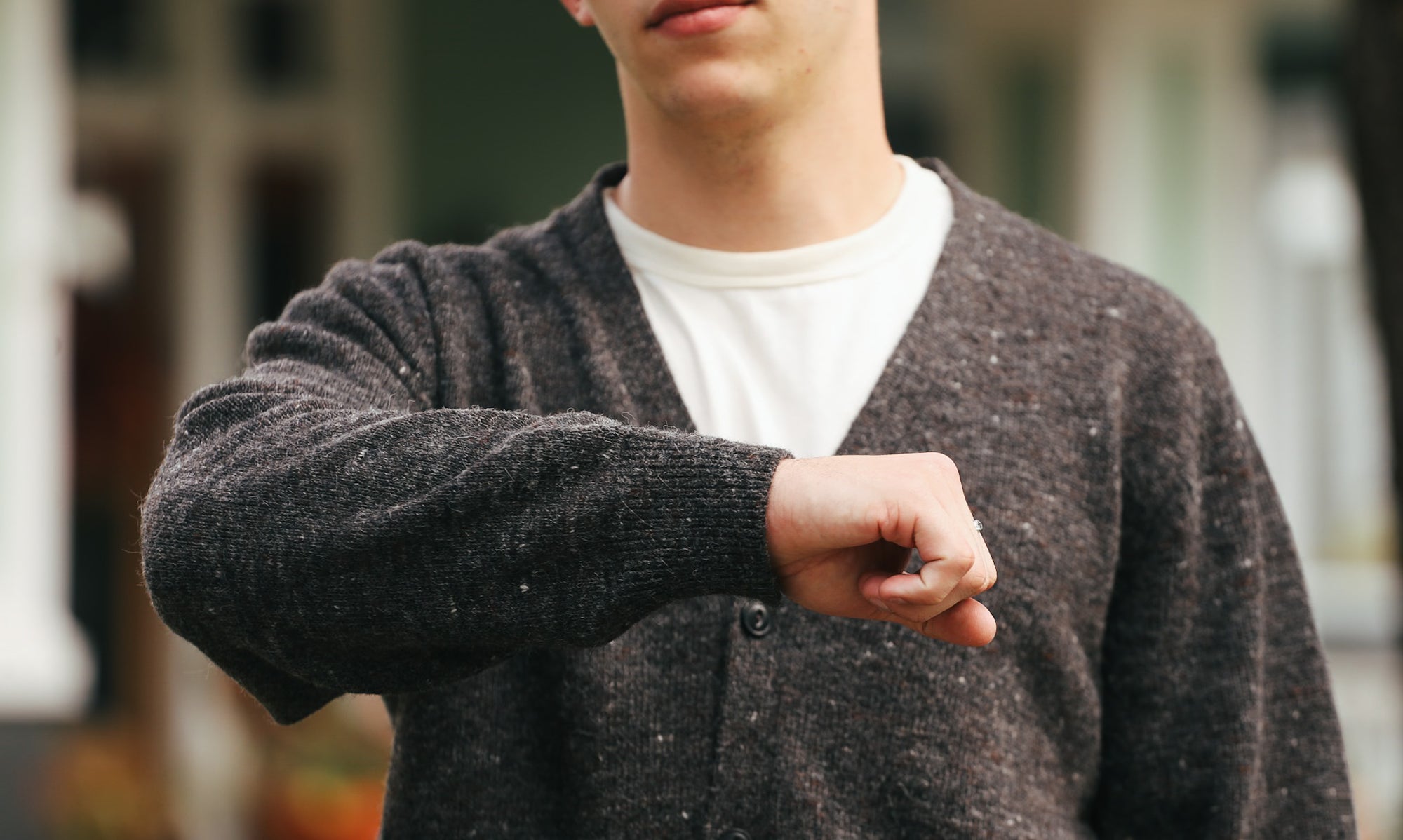 Man wearing dark knit cardigan and white shirt outdoors showing cuff and ring