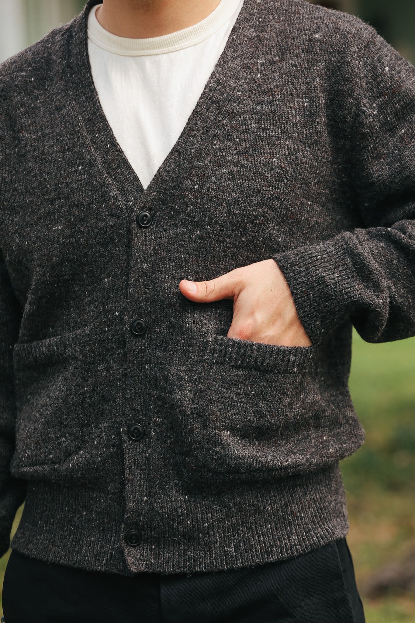 Close-up of a person wearing a dark grey button-up knit cardigan with hand in pocket over a white shirt