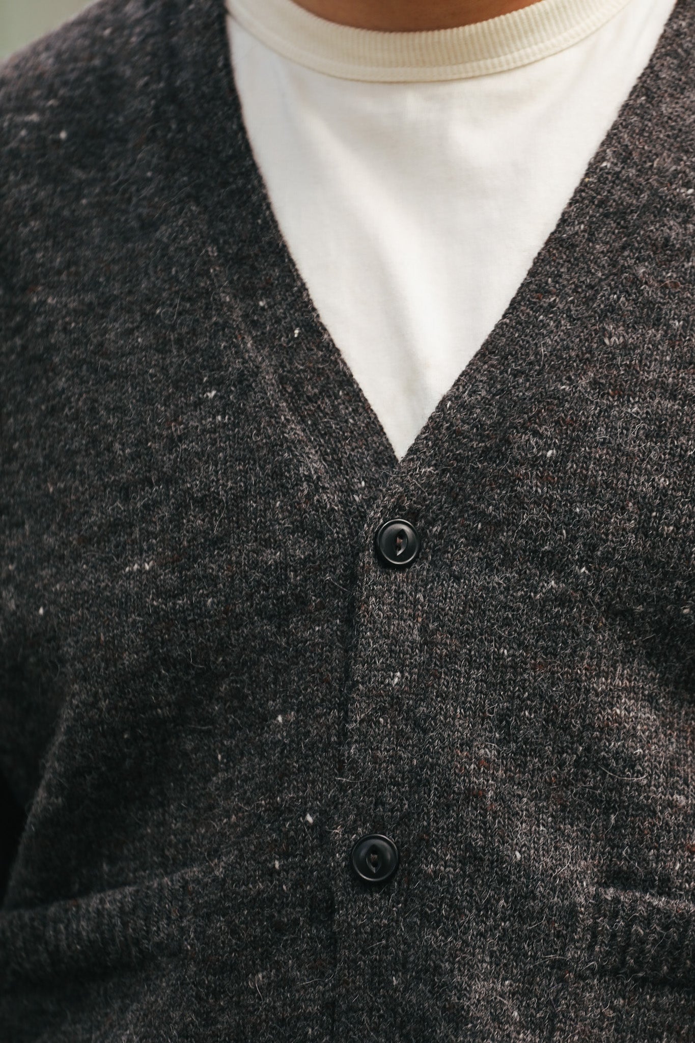 Close-up of dark wool knit cardigan with black buttons over white shirt, casual menswear