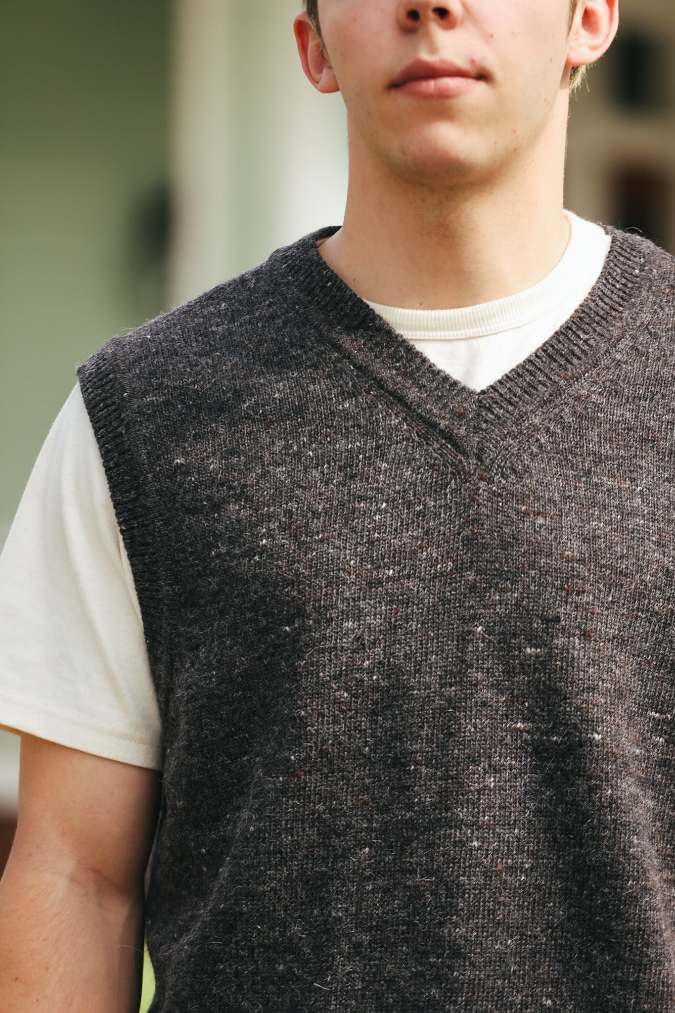 Close-up of a man wearing a dark gray knitted V-neck vest over a white T-shirt, Iron Shop Provisions style