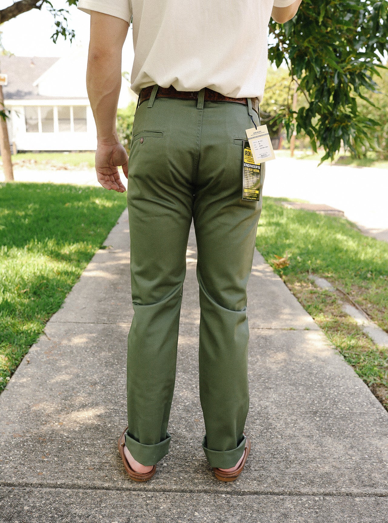 Man wearing olive green Iron Shop Provisions engineer pants with tags, standing on sidewalk outdoors