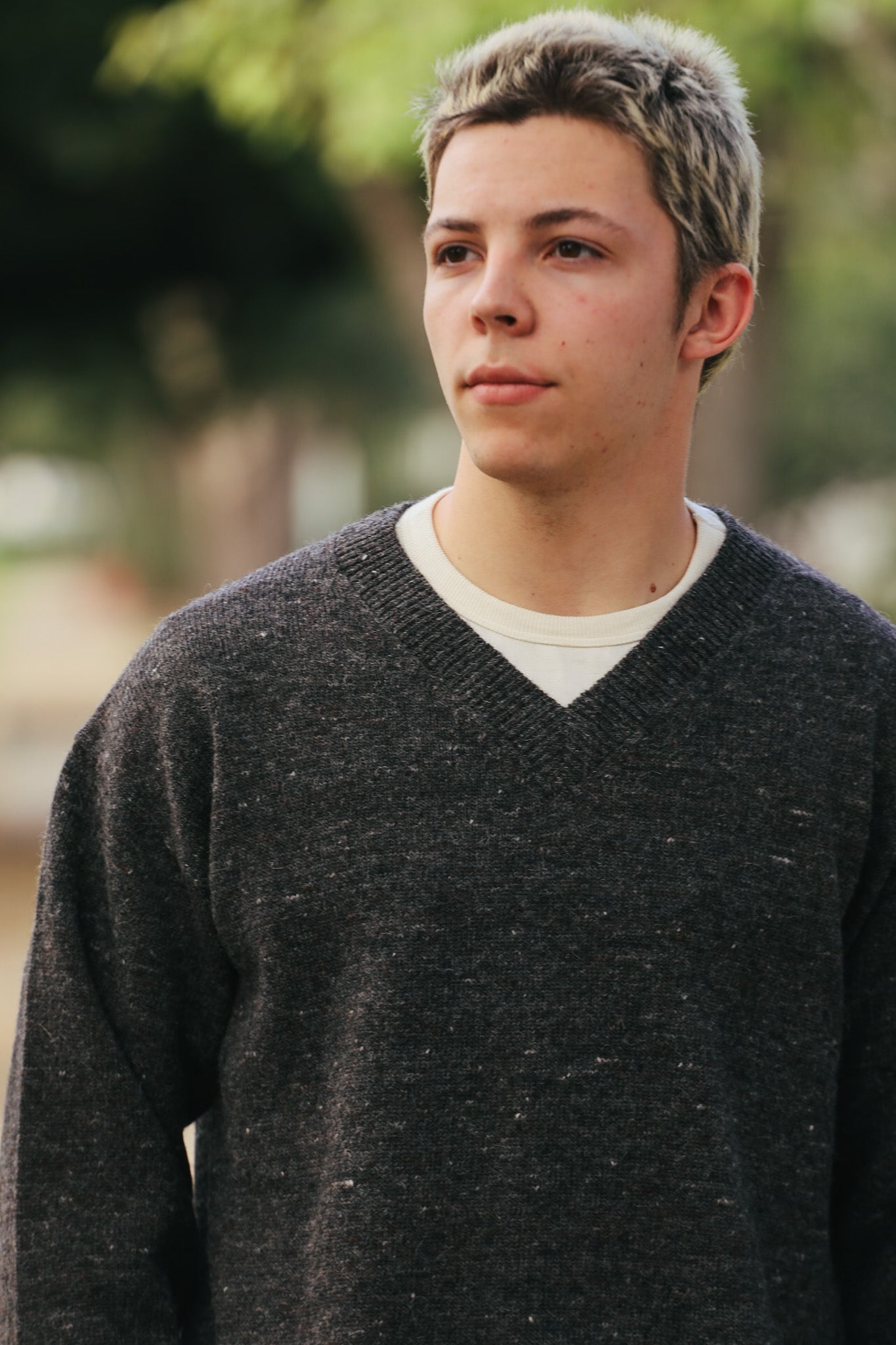 Young man wearing dark charcoal wool V-neck sweater over white shirt outdoors
