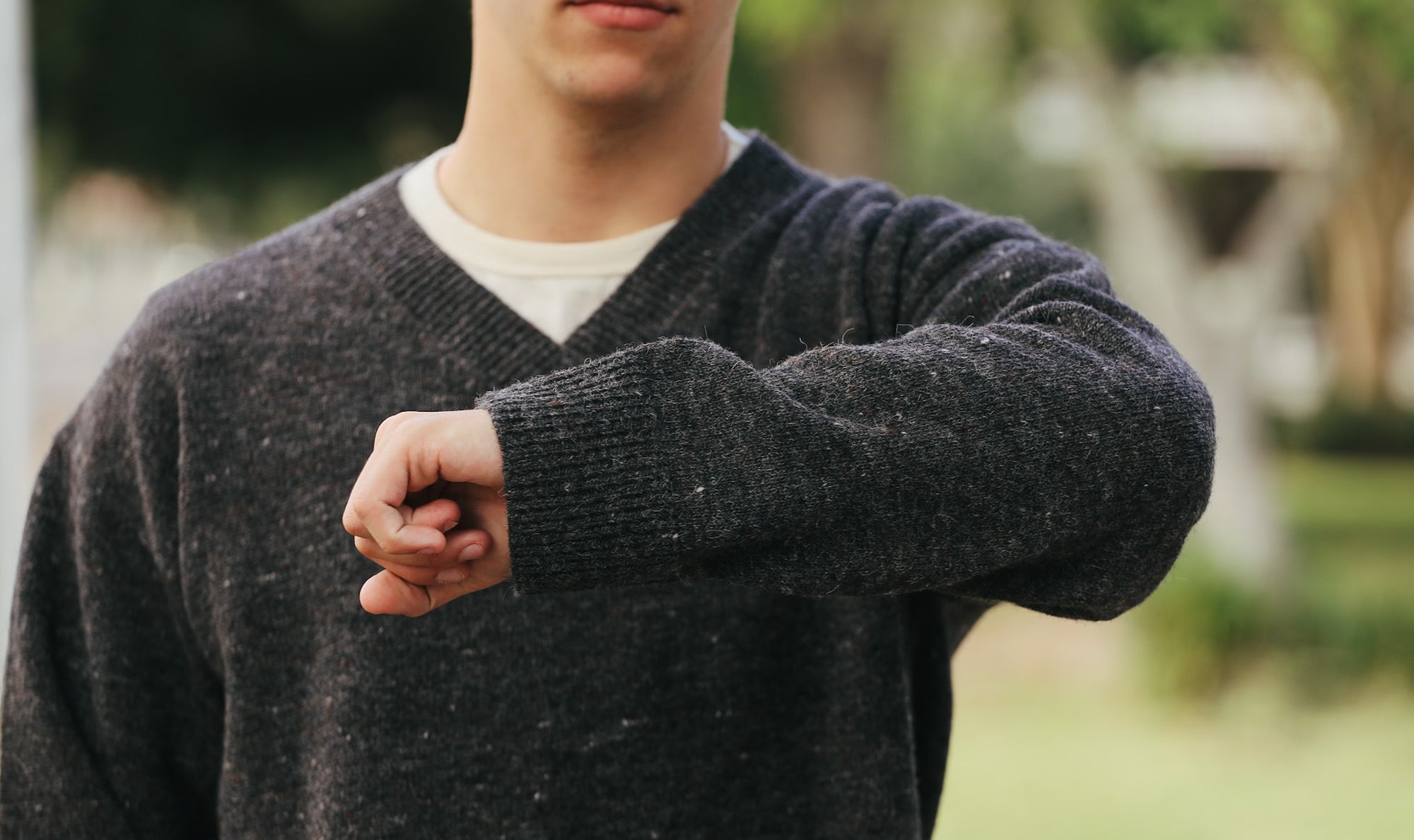 Close-up of a person wearing a dark gray knitted sweater outdoors with a blurred green background