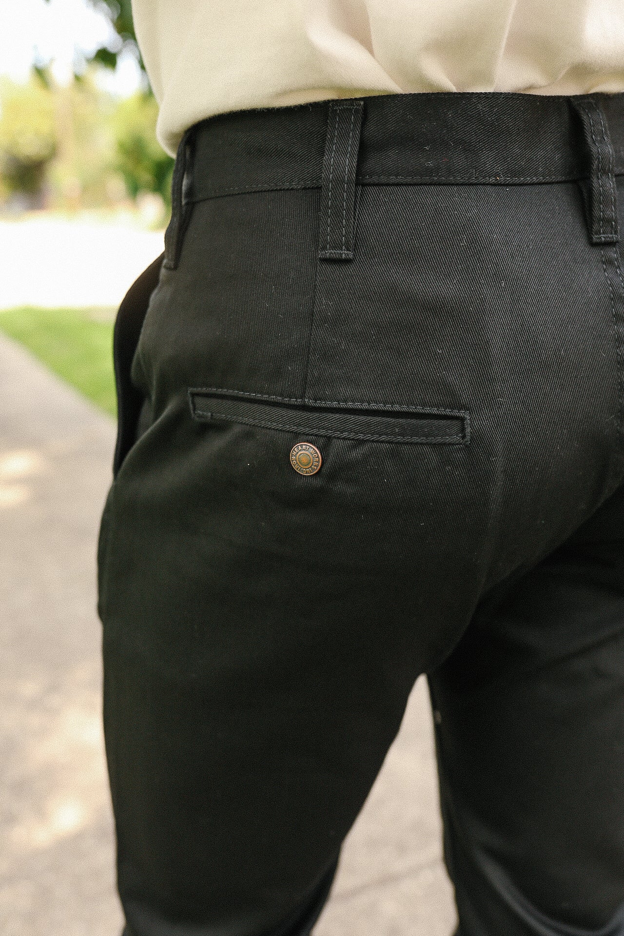 Close-up of black denim pants back pocket with branded rivet in outdoor setting