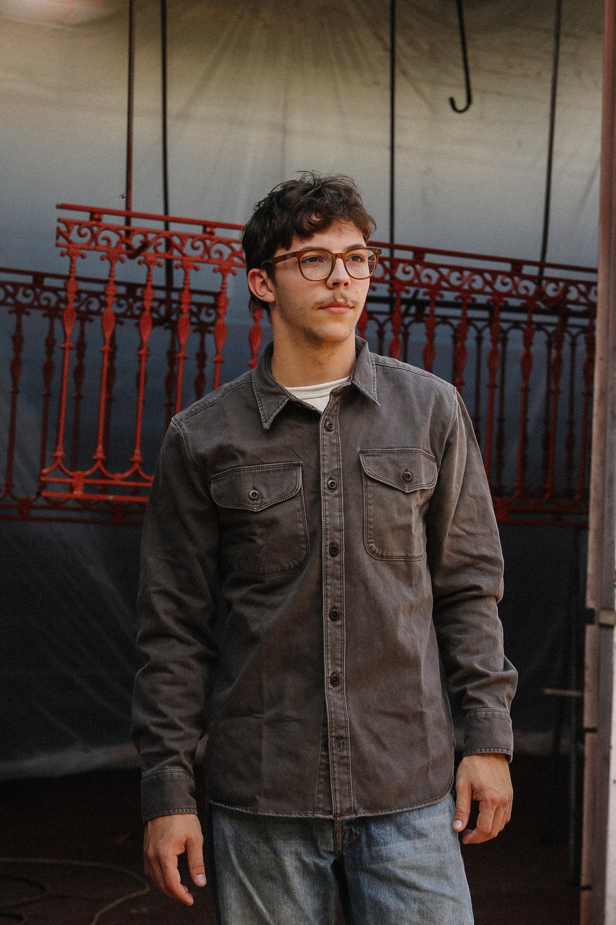 man wearing brown shirt standing in front of metal gate