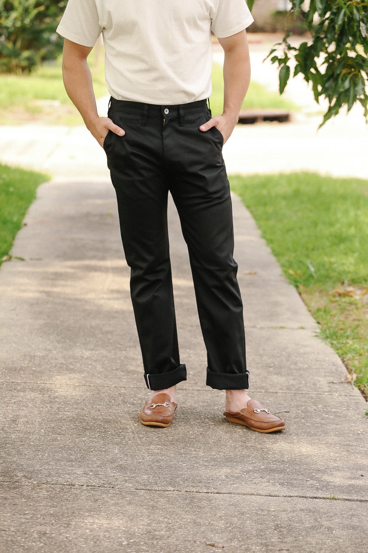 Man wearing black trousers with cuffs and brown slip-on loafers standing on outdoor pathway