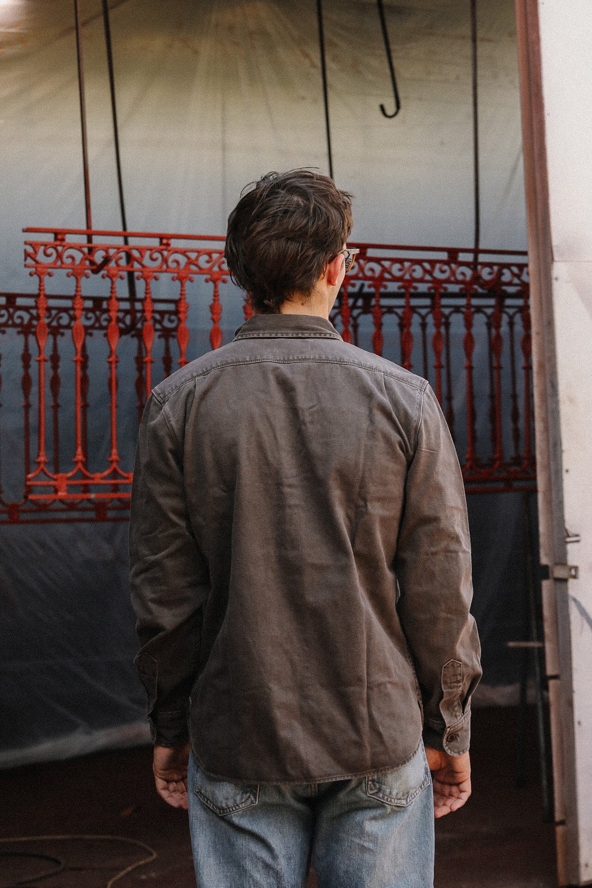 man wearing brown shirt standing in front of metal gate