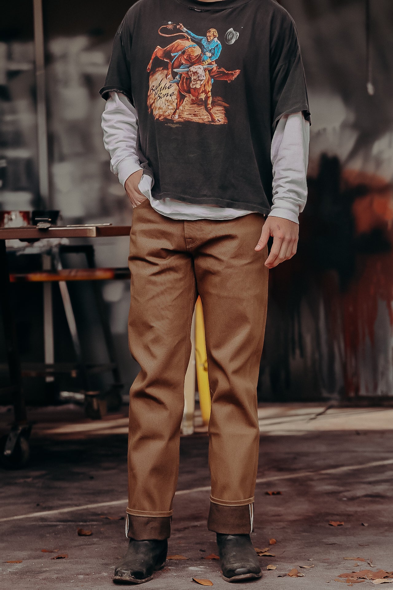 Person wearing brown work pants, black boots, layered white long sleeve and black graphic tee with cowboy design